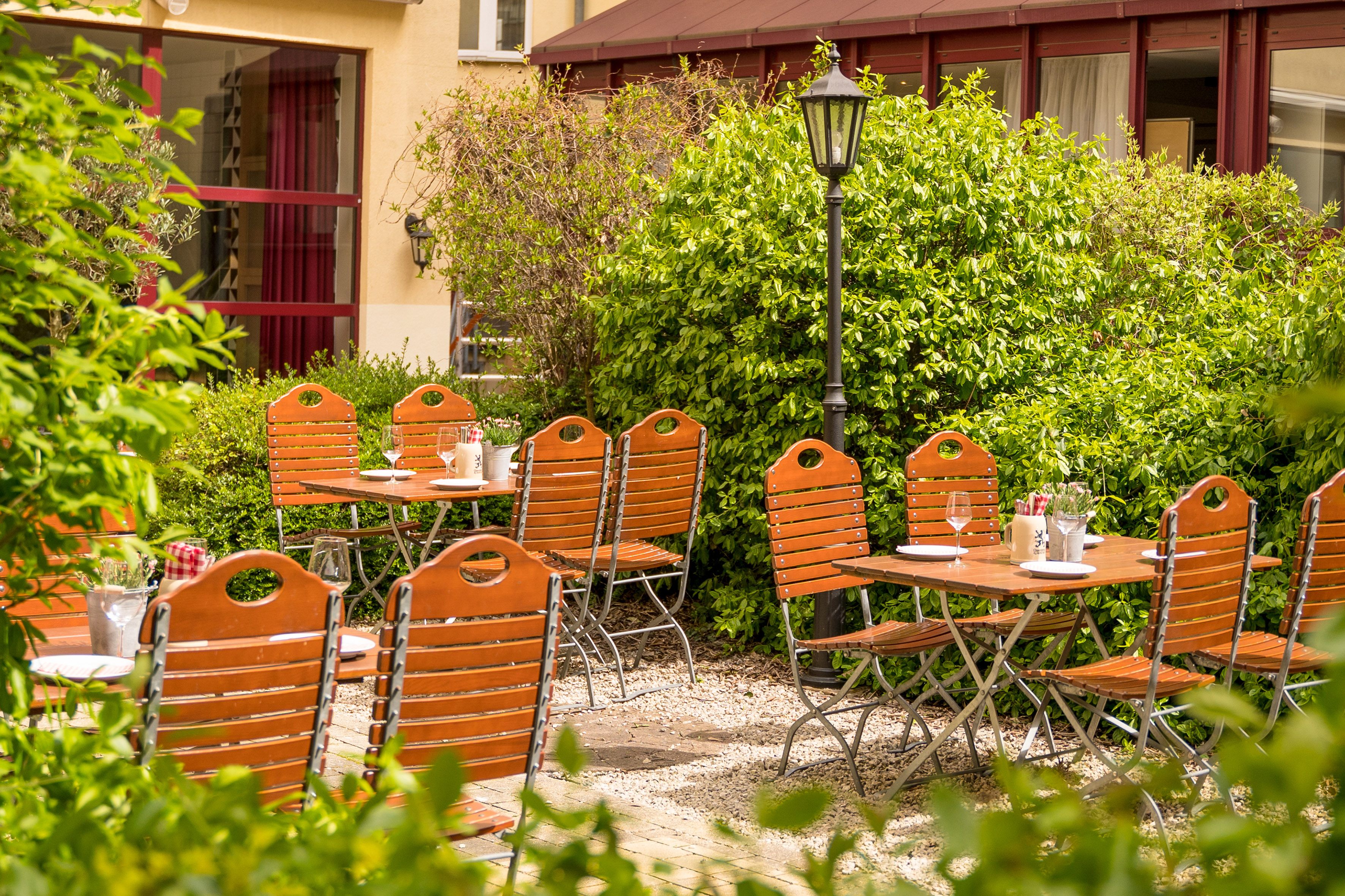 Outdoor dining tables and chairs in a green garden courtyard.