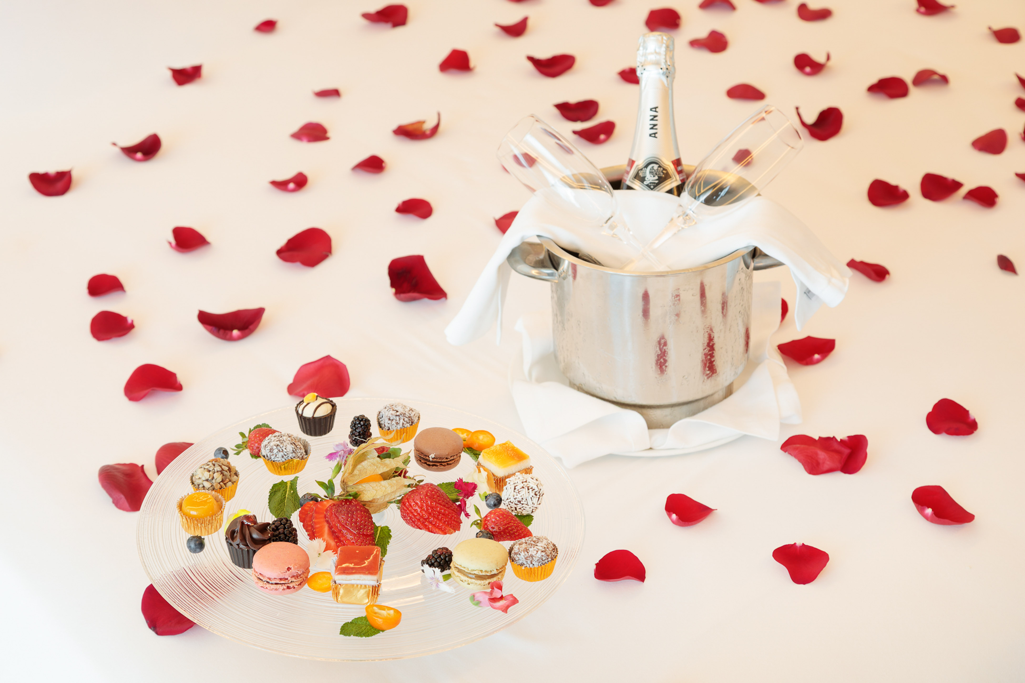 Champagne, desserts, and rose petals on white, for a romantic celebration.
