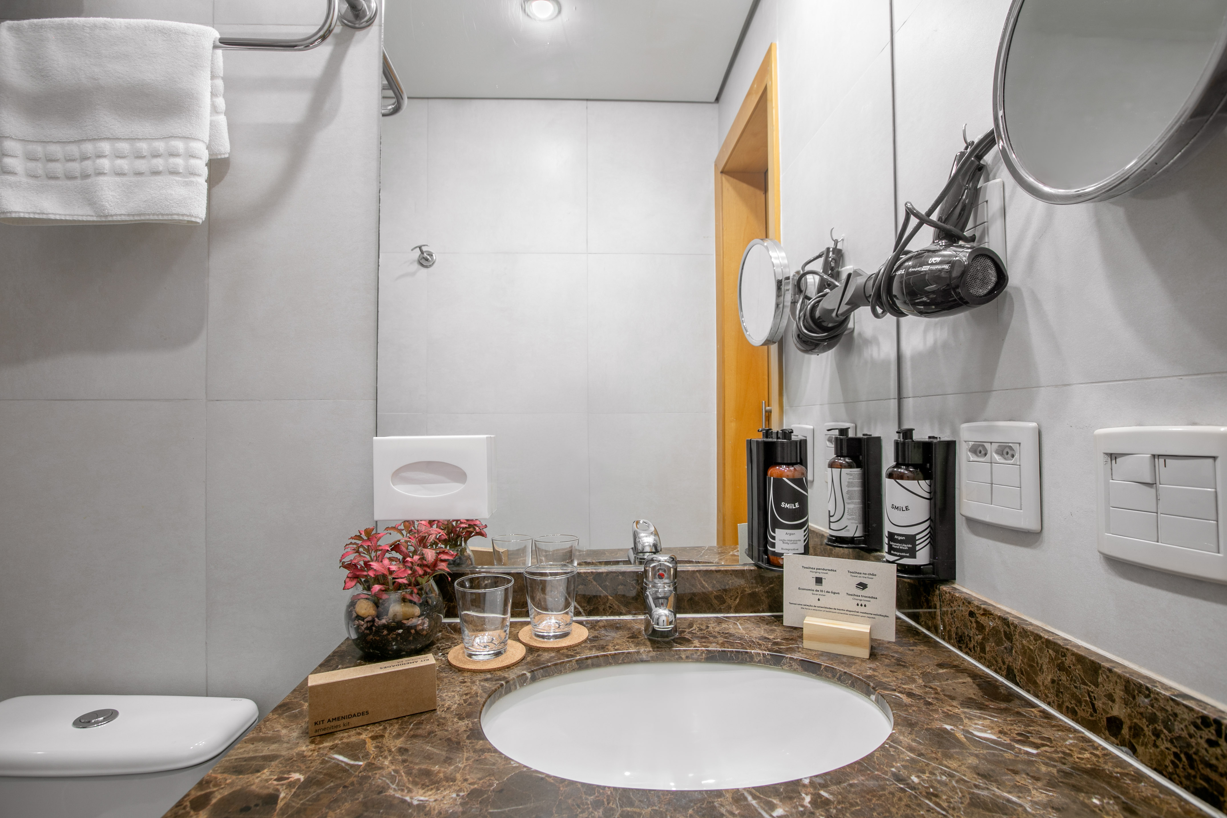 Modern hotel bathroom vanity with marble countertop, sink, mirror, toiletries, and hairdryer.
