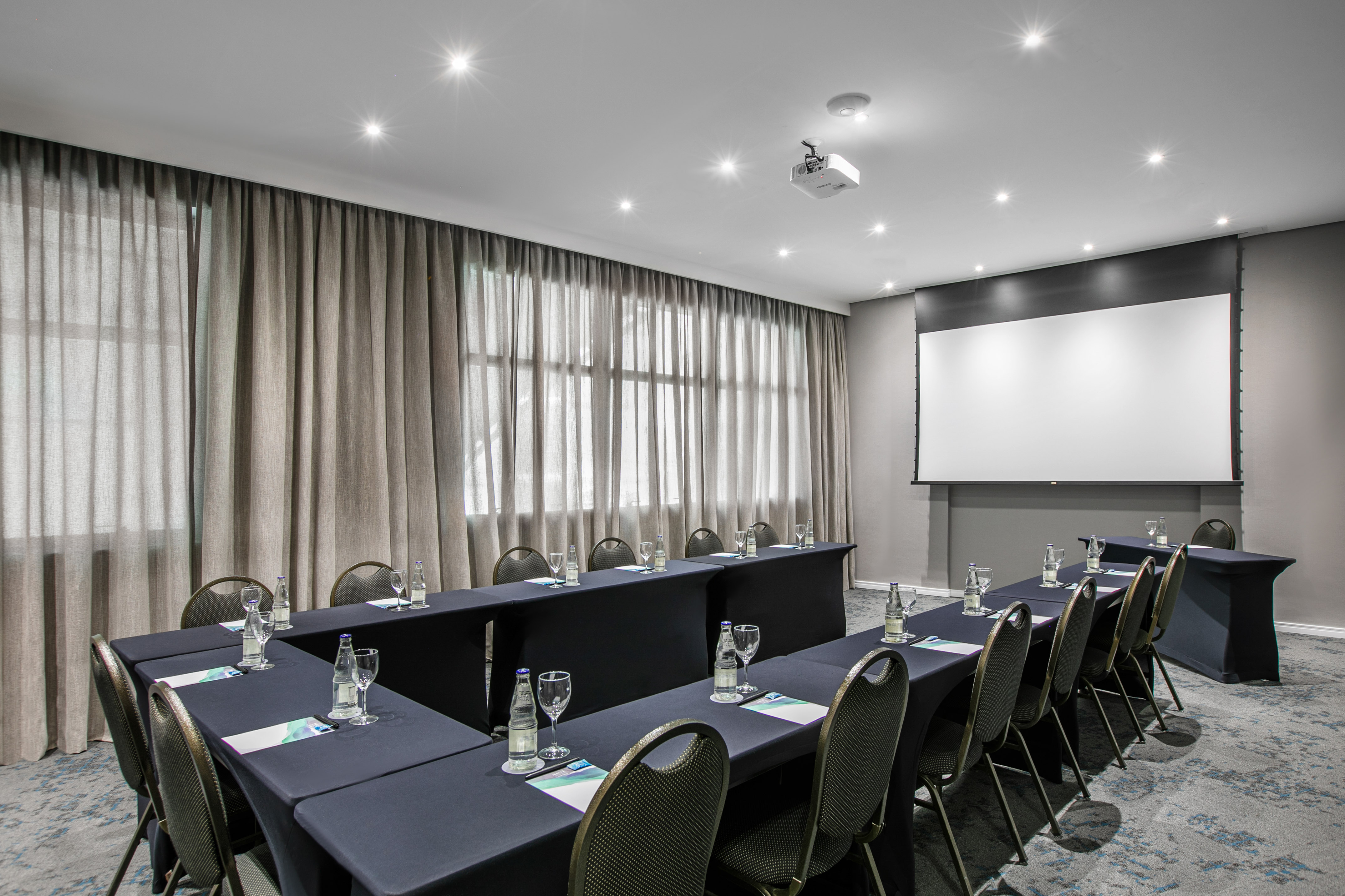 Modern conference room with U-shape table setup, projector screen.