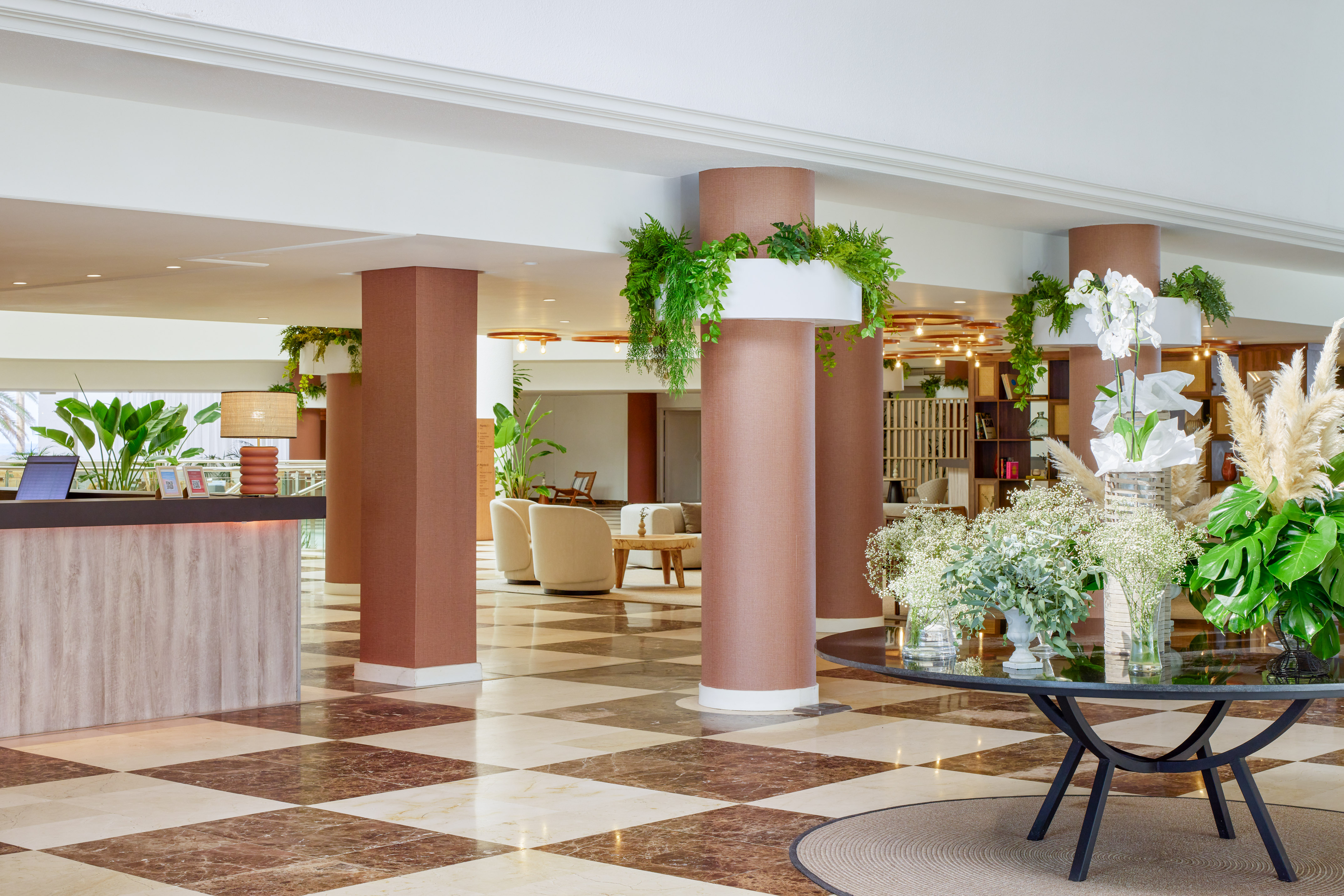 Hotel lobby with reception desk, checkered marble floor, and lush plants.