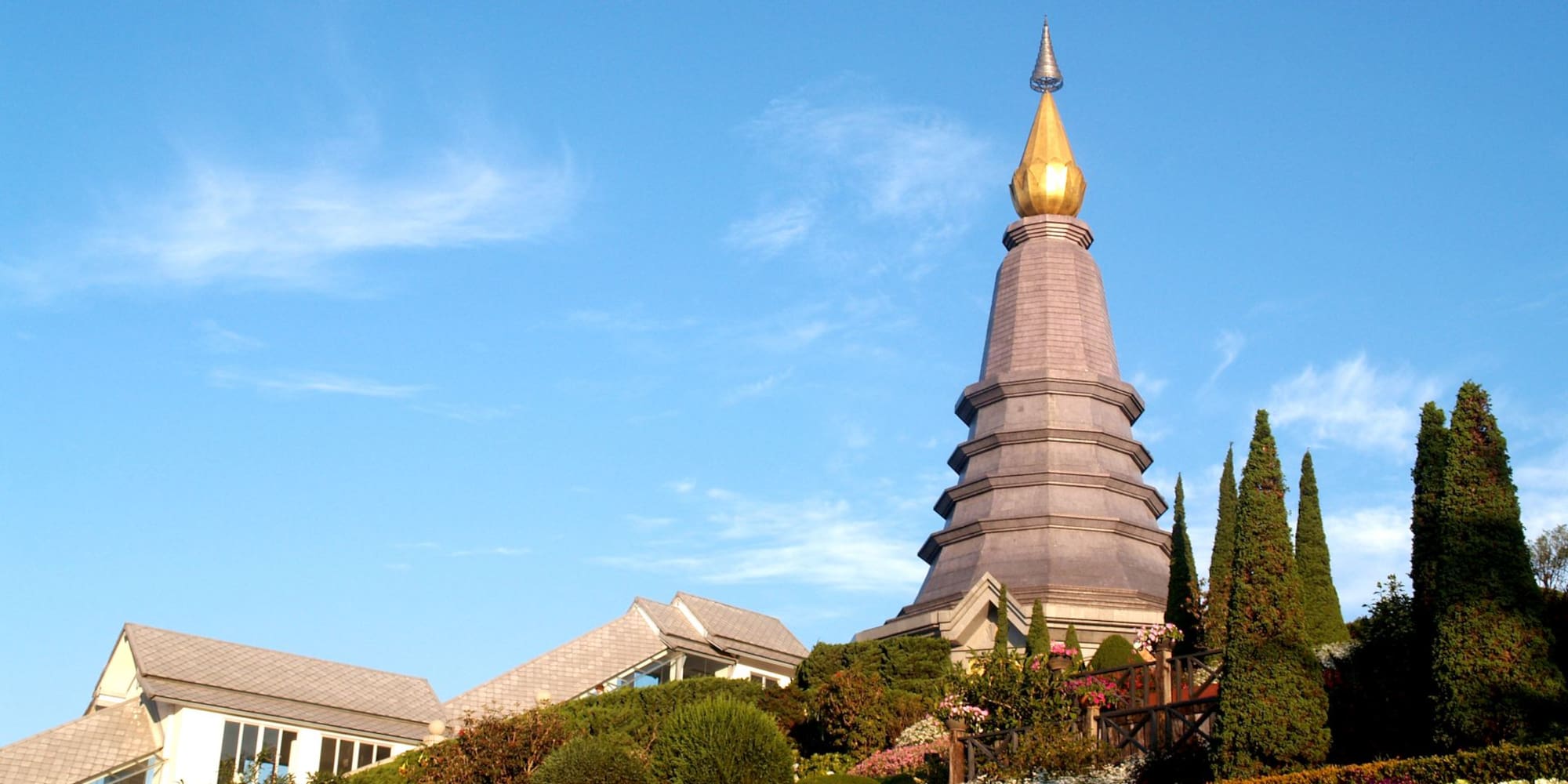 Thai pagoda with golden spire, vibrant flowers in hillside gardens.