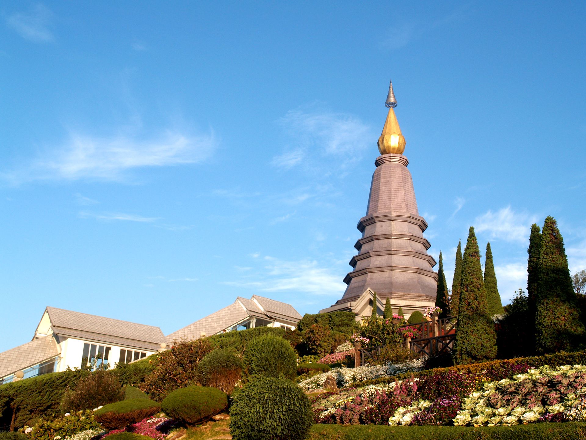 Thai pagoda with golden spire, vibrant flowers in hillside gardens.