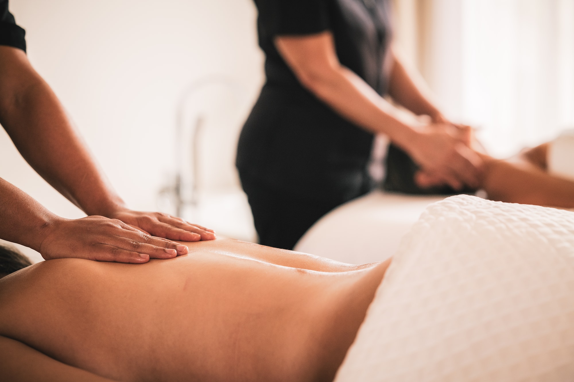 Hands giving a back massage to a person in a serene spa.