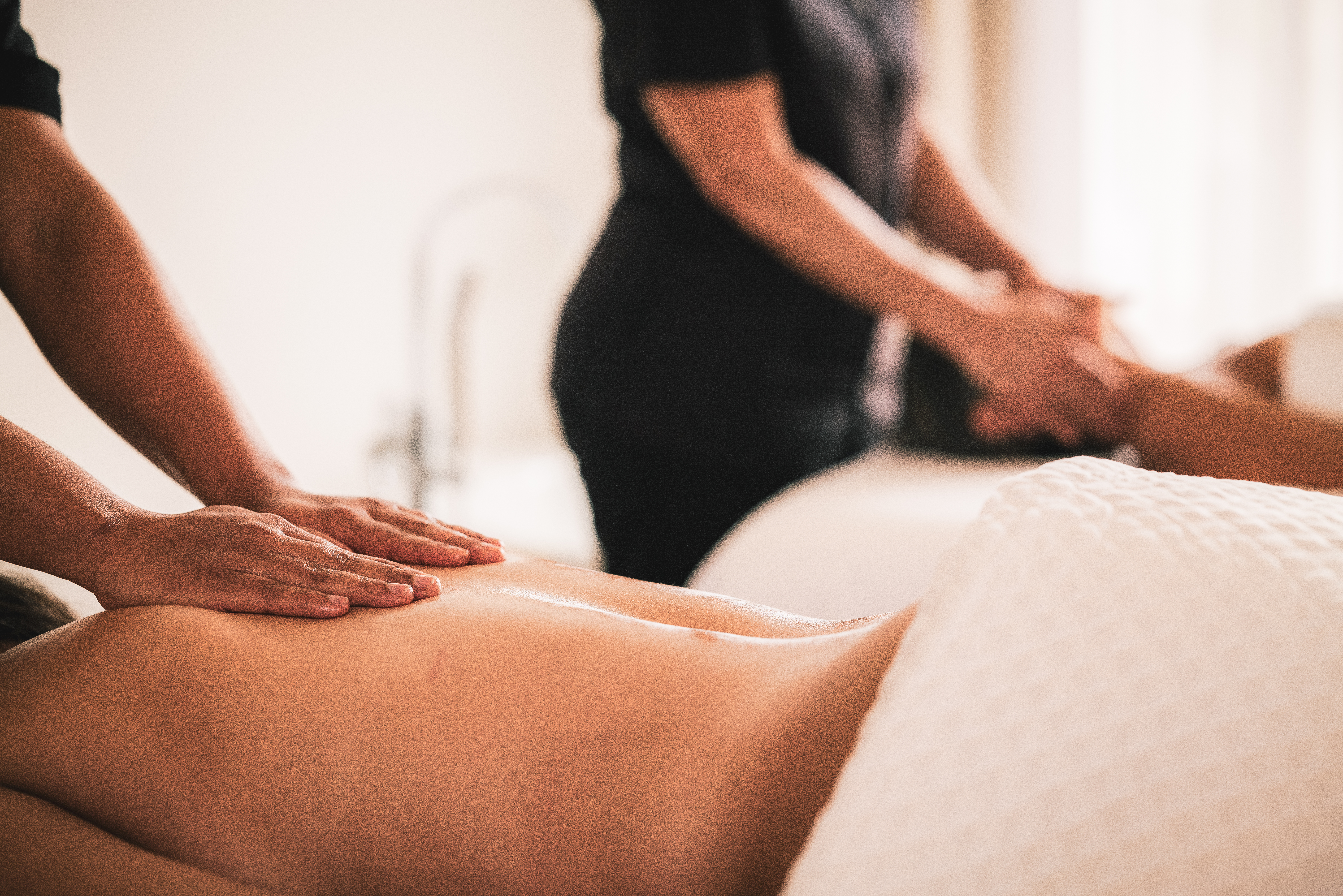 Hands giving a back massage to a person in a serene spa.