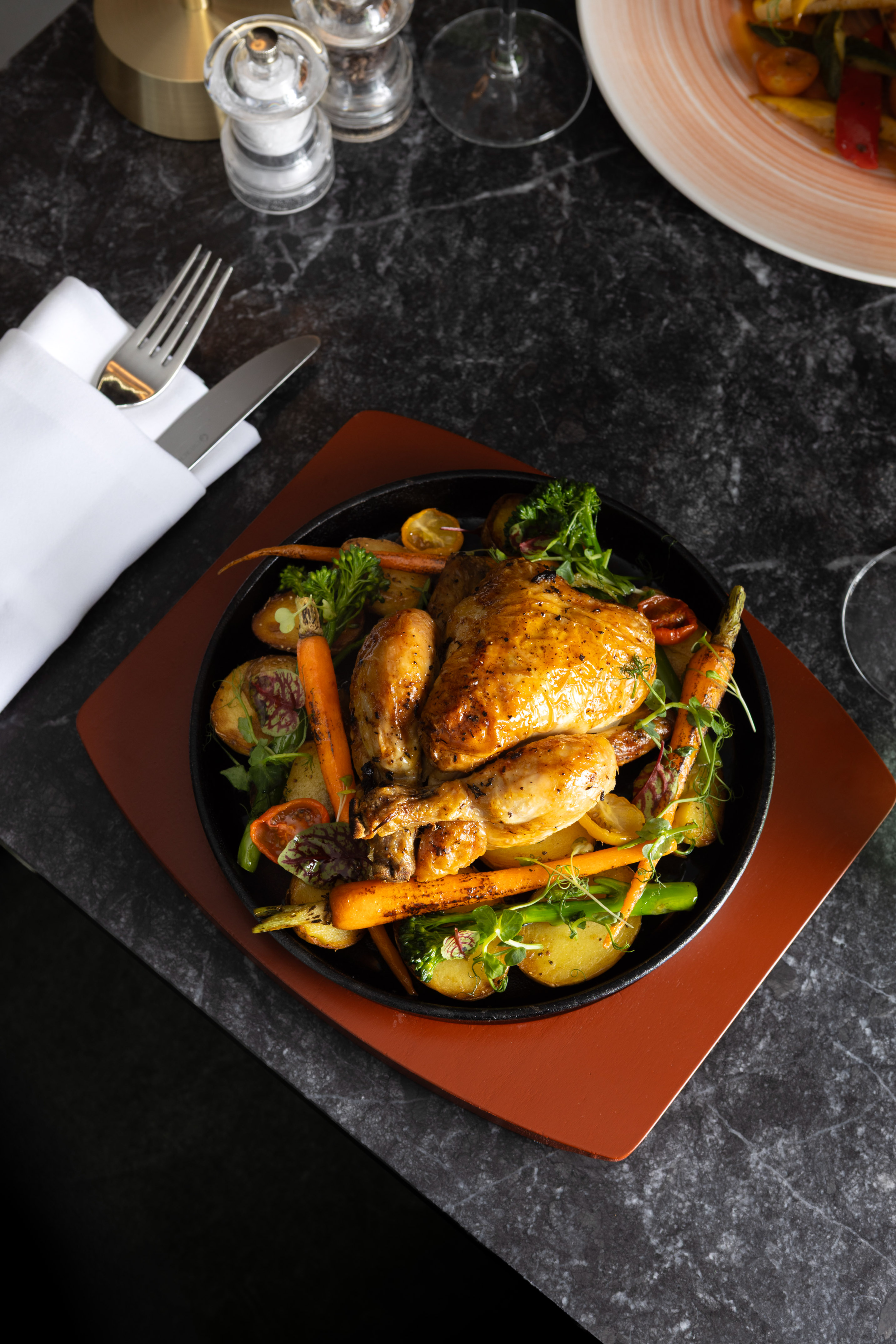 Gourmet roasted chicken with potatoes and carrots, served in a black skillet.