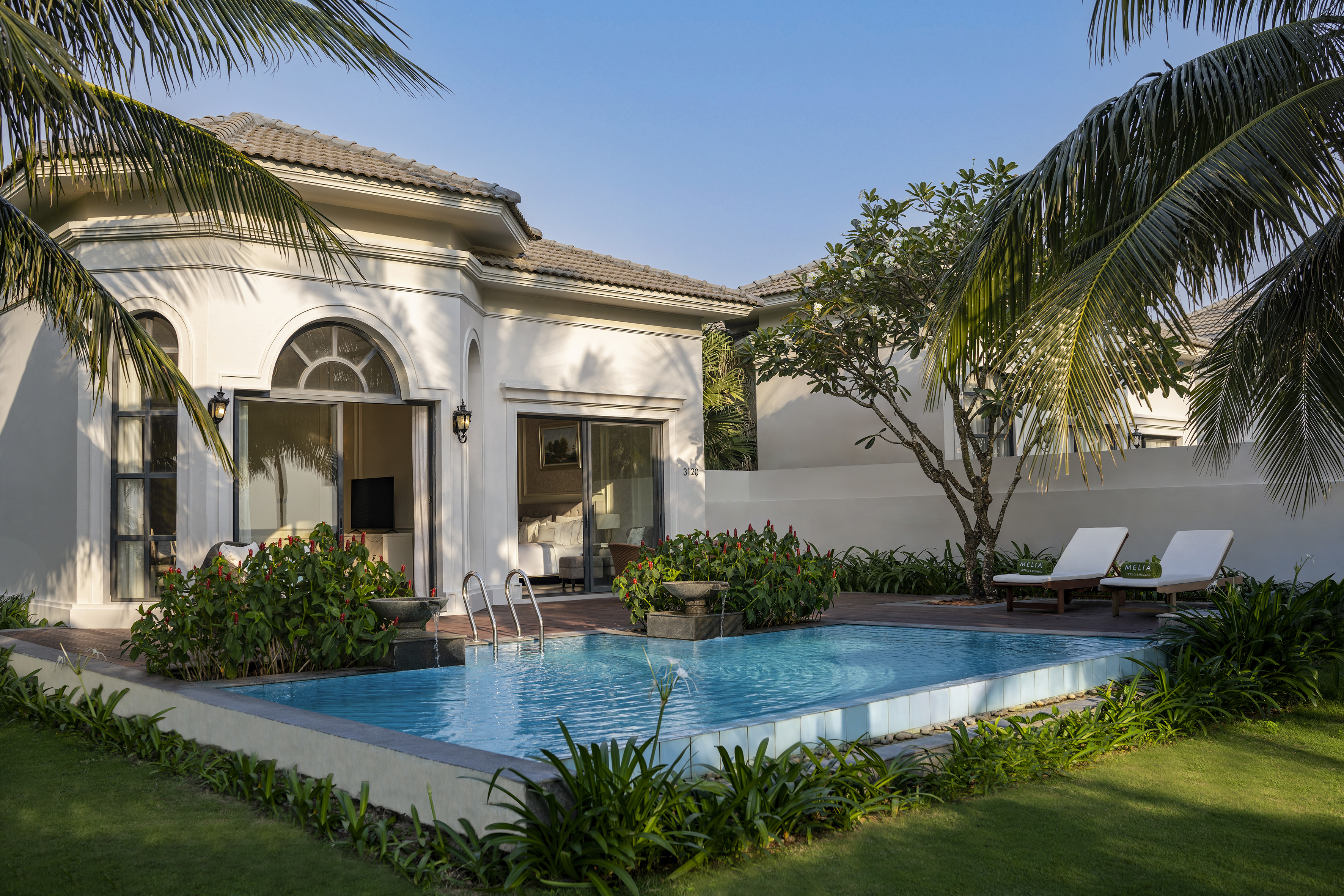 White resort villa with private pool, tropical garden, and palm trees.