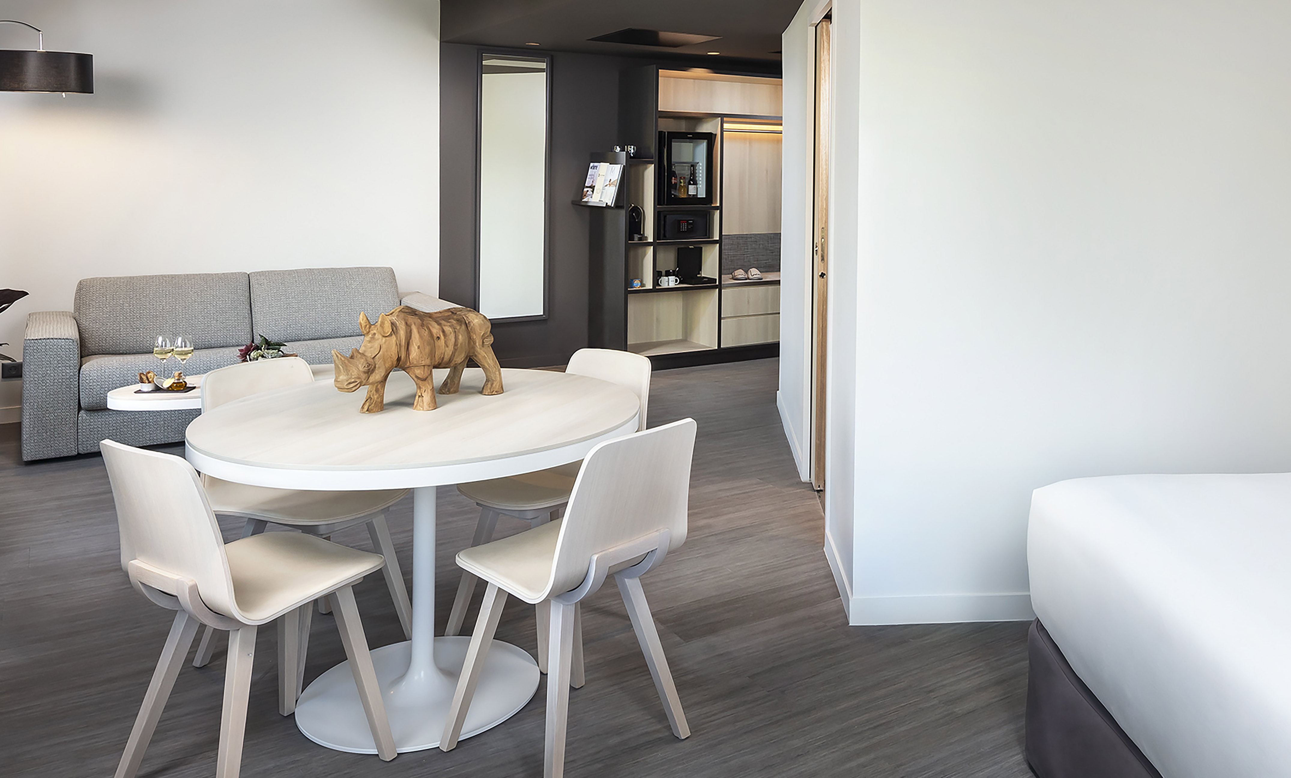 Modern hotel suite living area with dining table, sofa, and kitchenette.