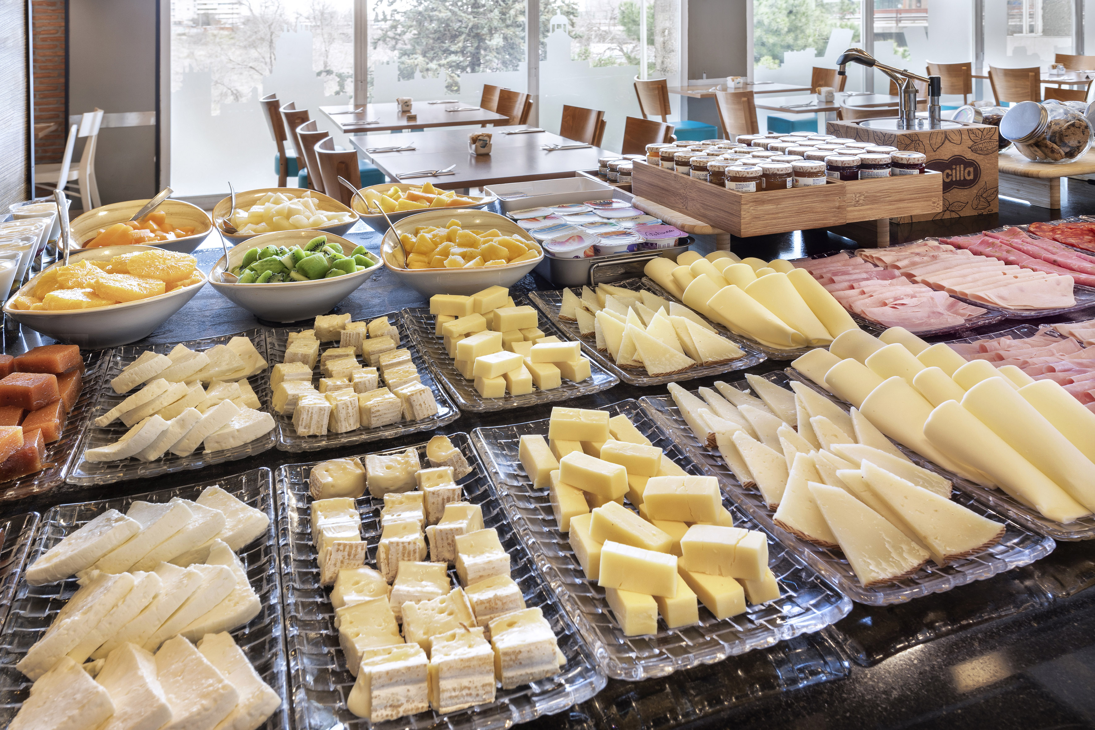 Hotel breakfast buffet with cheese, ham, fresh fruit, yogurt, and jams.