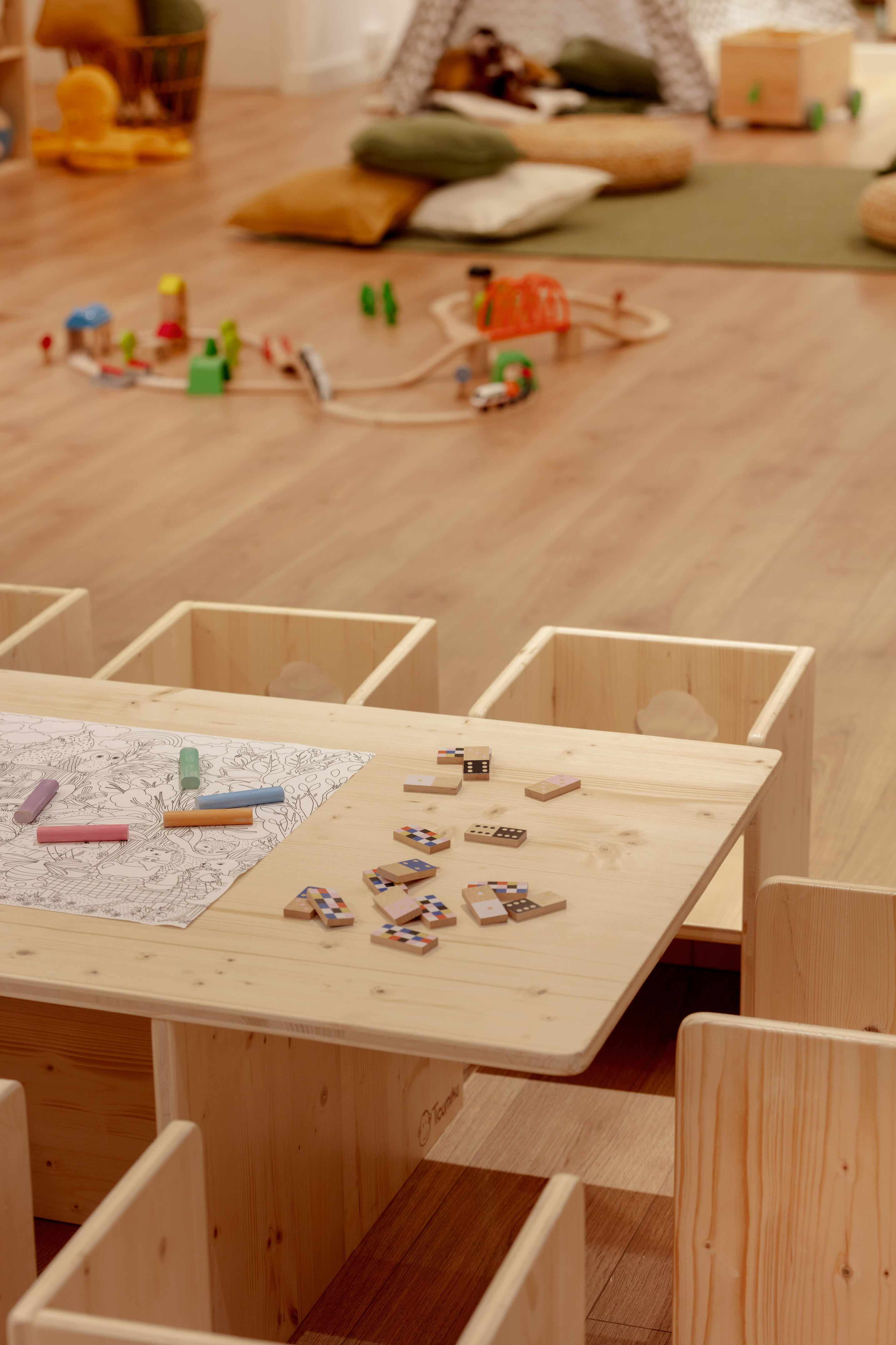 Wooden children's table with coloring page, crayons, dominoes in a playroom.