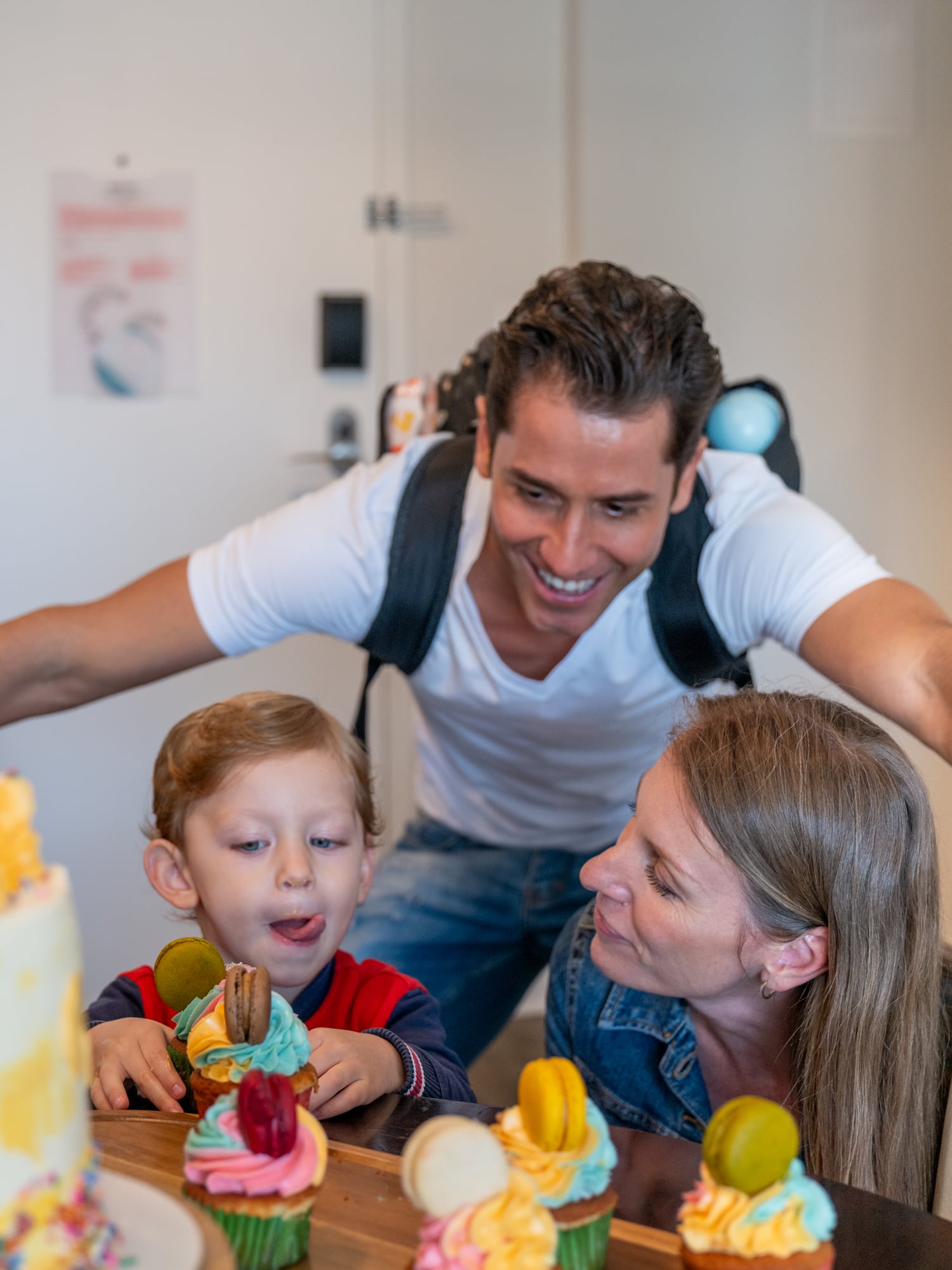 Smiling family, young son eagerly looking at colorful birthday cupcakes.