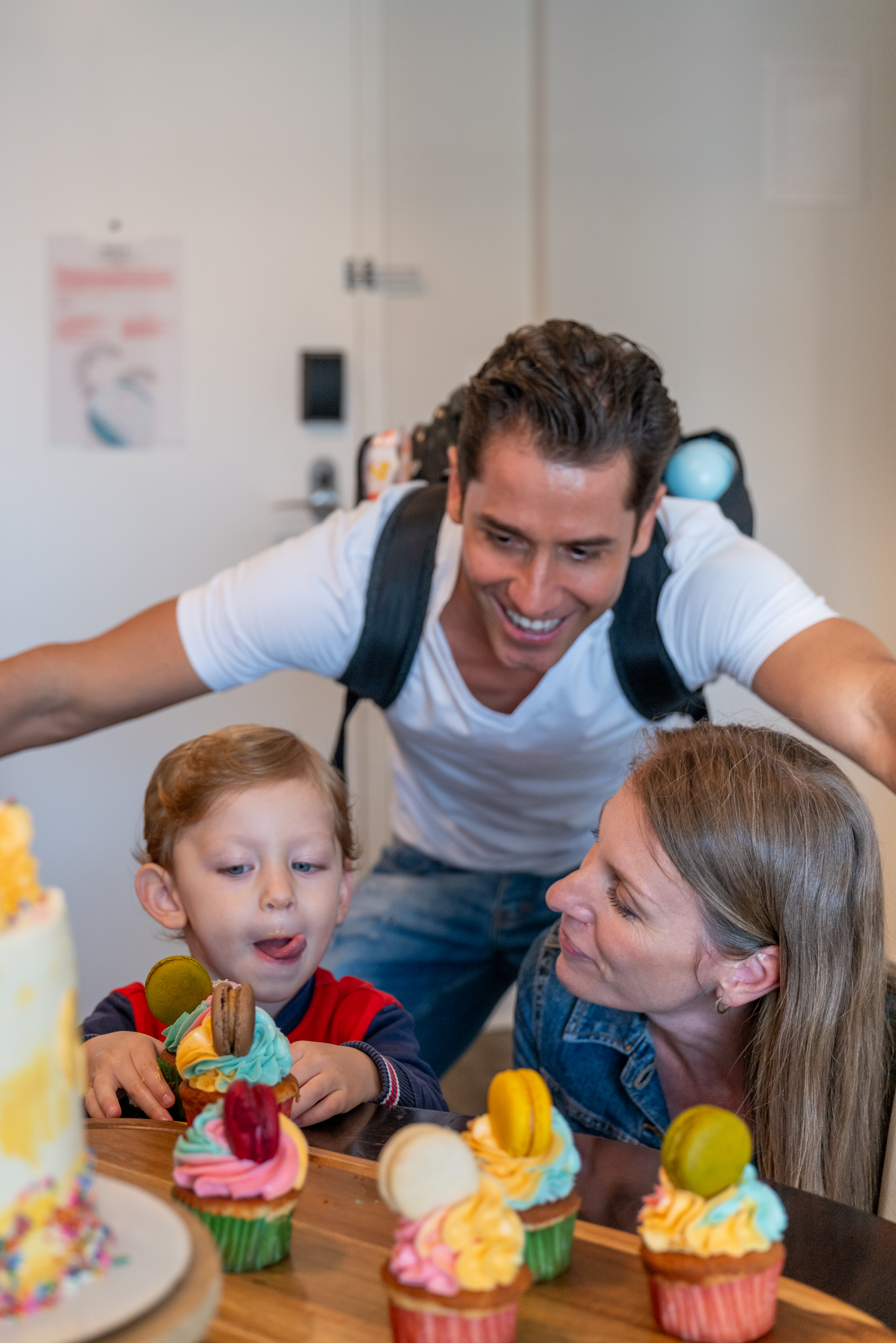 Smiling family, young son eagerly looking at colorful birthday cupcakes.