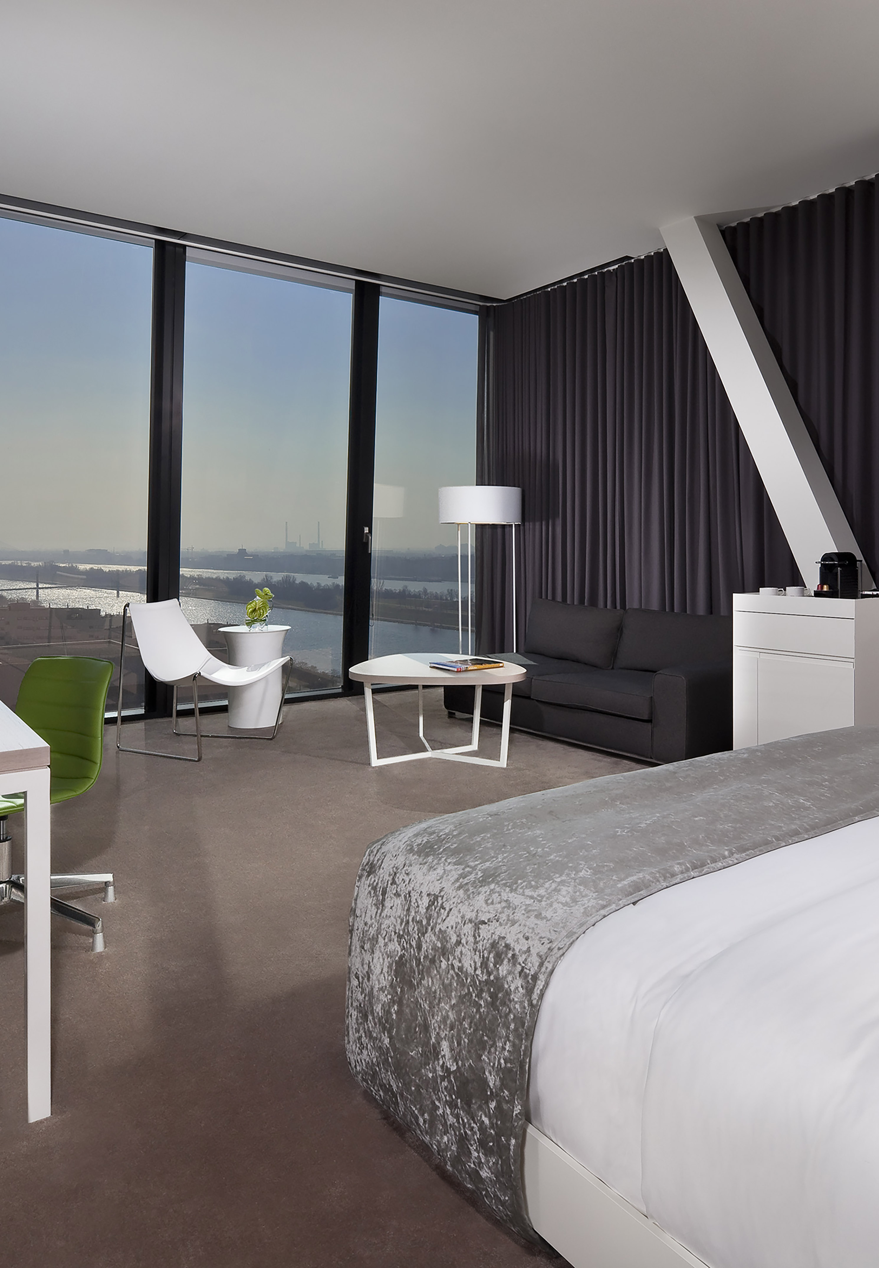 Upscale hotel suite with panoramic river view, bed, sofa, and workspace.