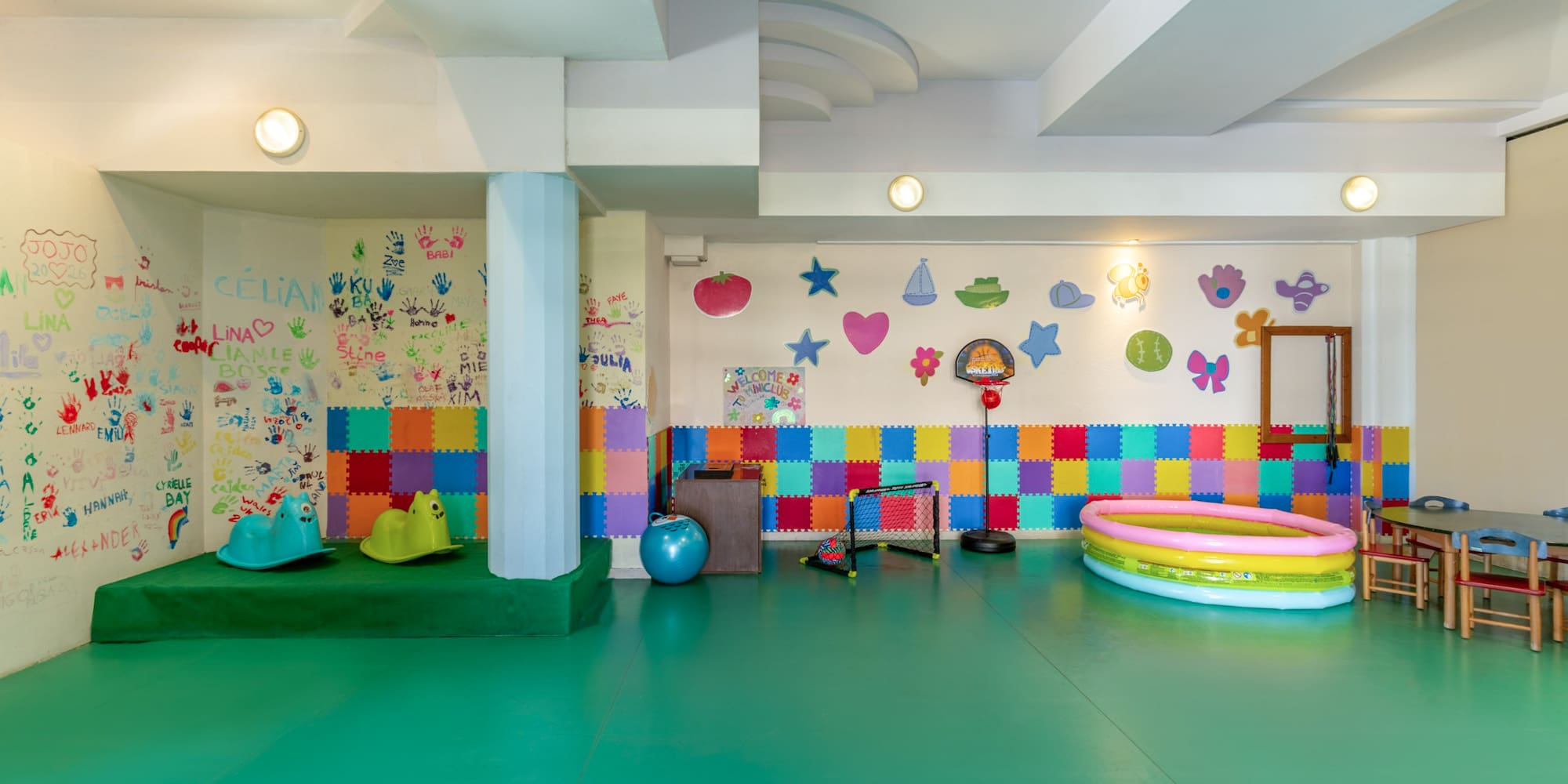 Colorful children's playroom with green floor, handprint wall, and play equipment.