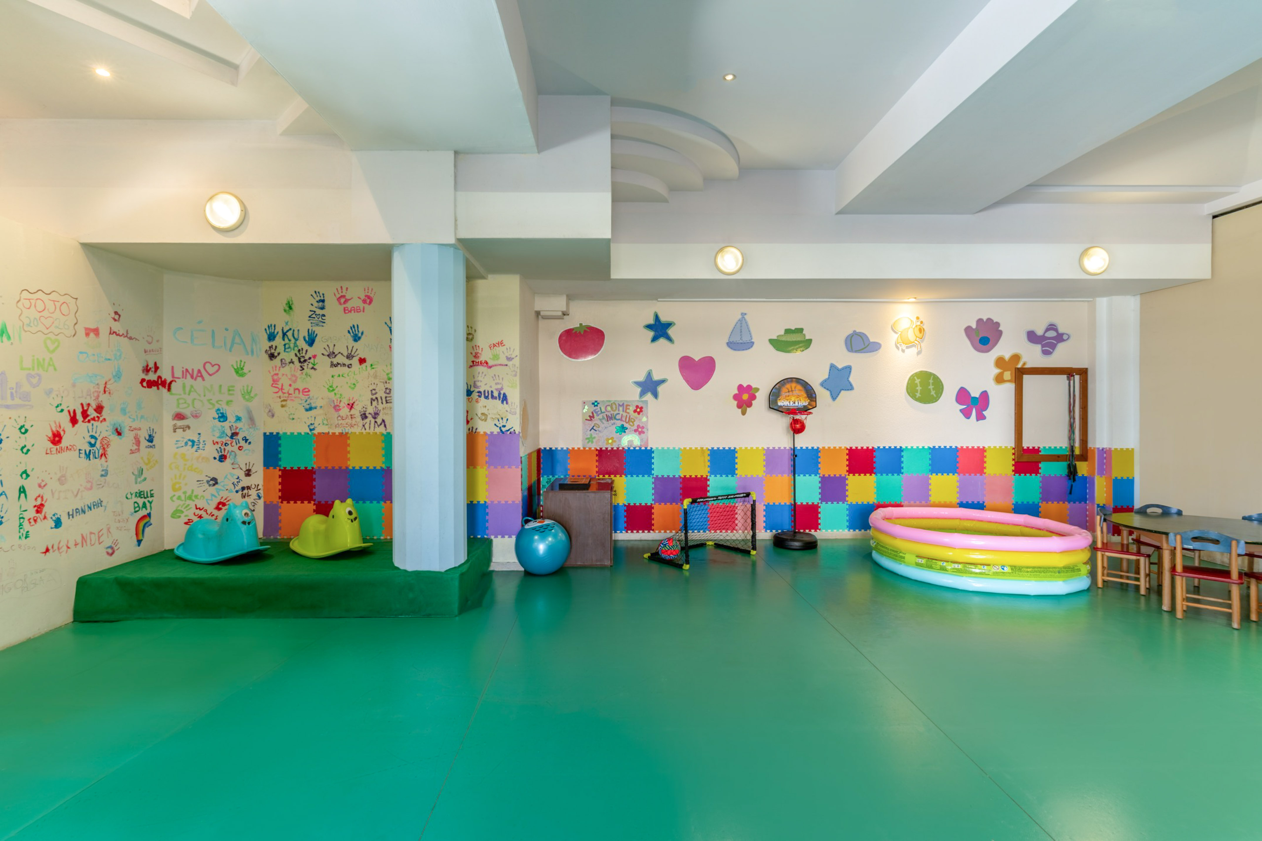 Colorful children's playroom with green floor, handprint wall, and play equipment.
