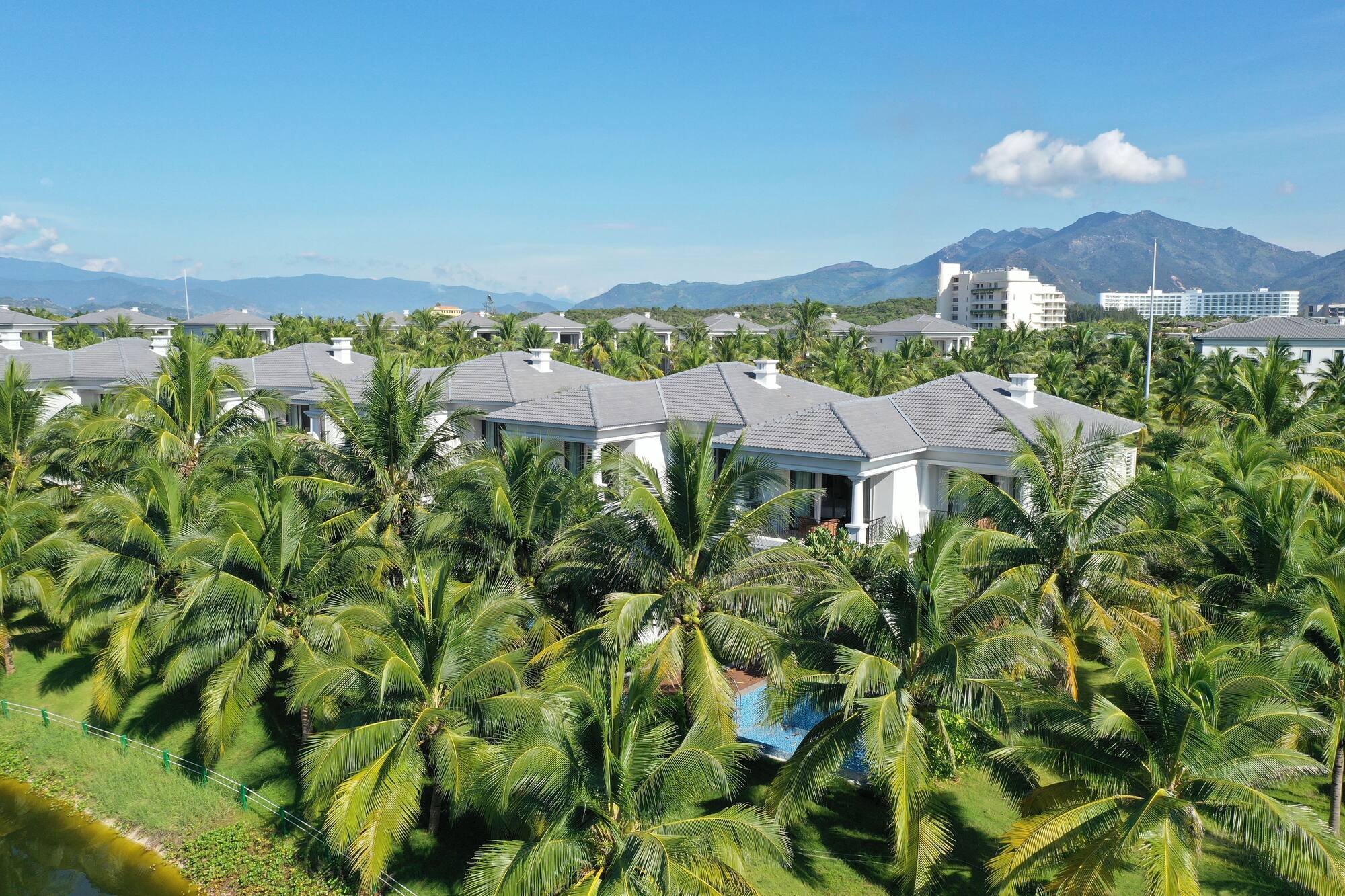 Tropical resort villas, palm trees, mountains, and clear blue sky.