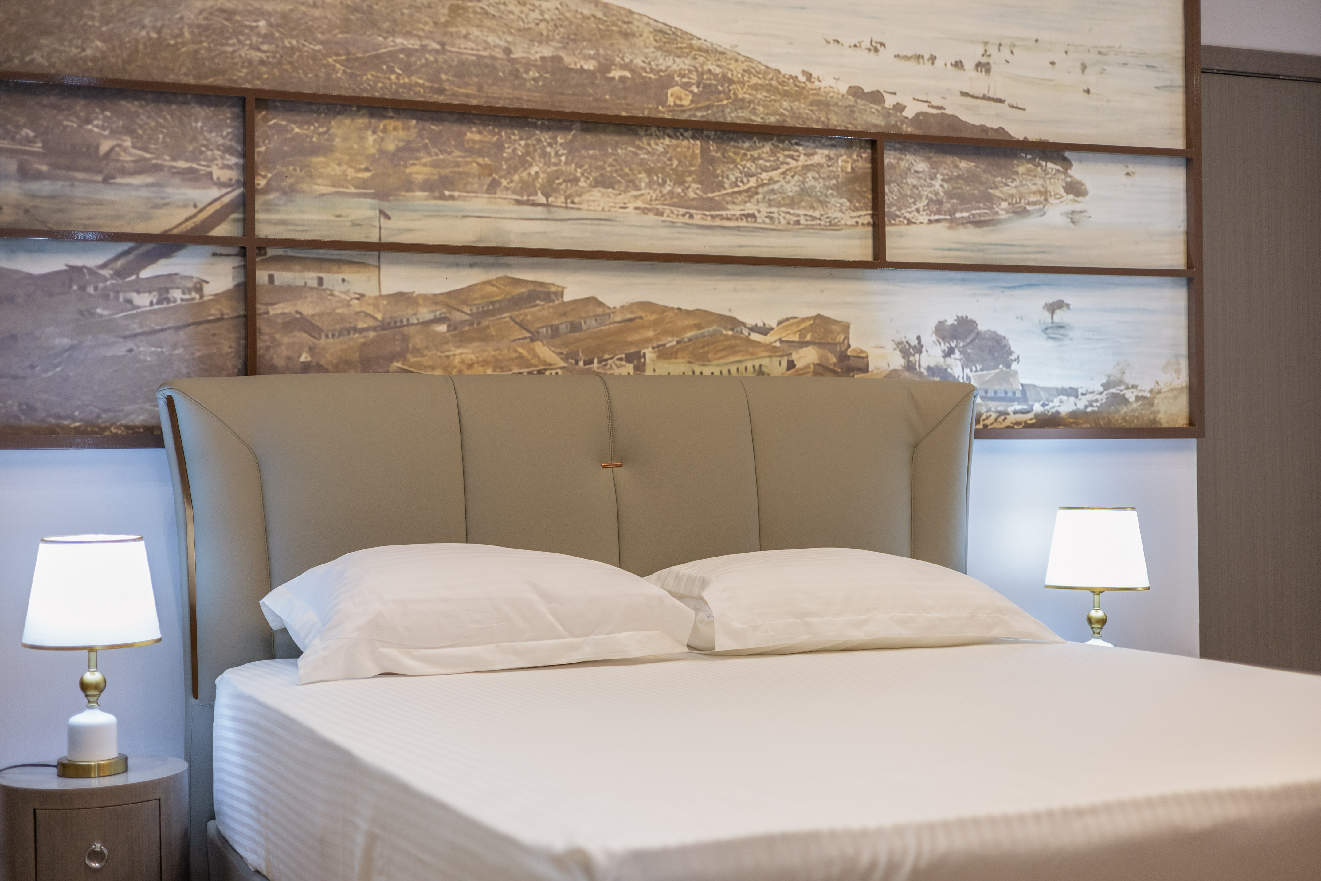 Hotel room with bed, upholstered headboard, lamps, and panoramic wall art.