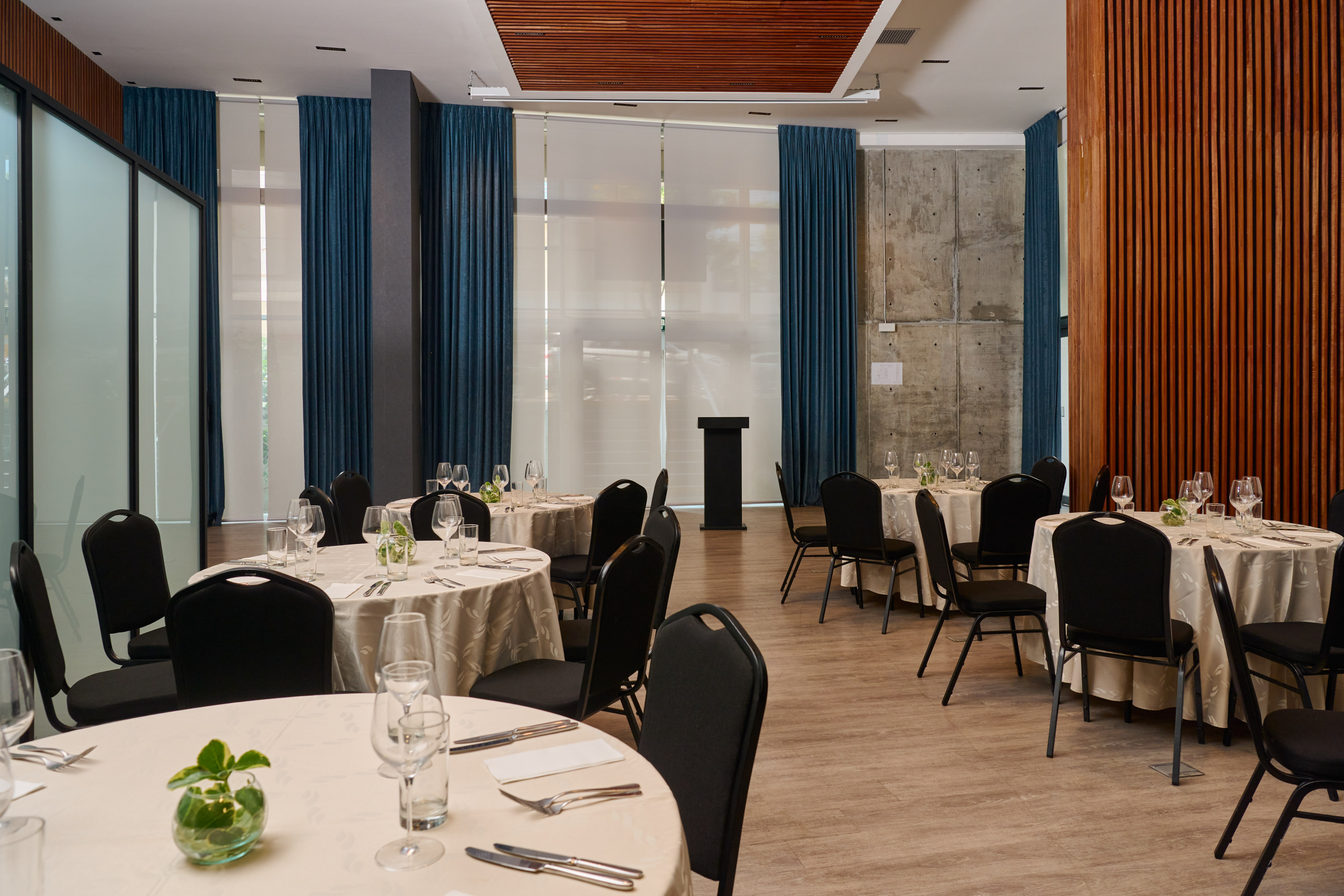 Modern banquet hall with round tables, black chairs, podium, and wood-paneled walls.