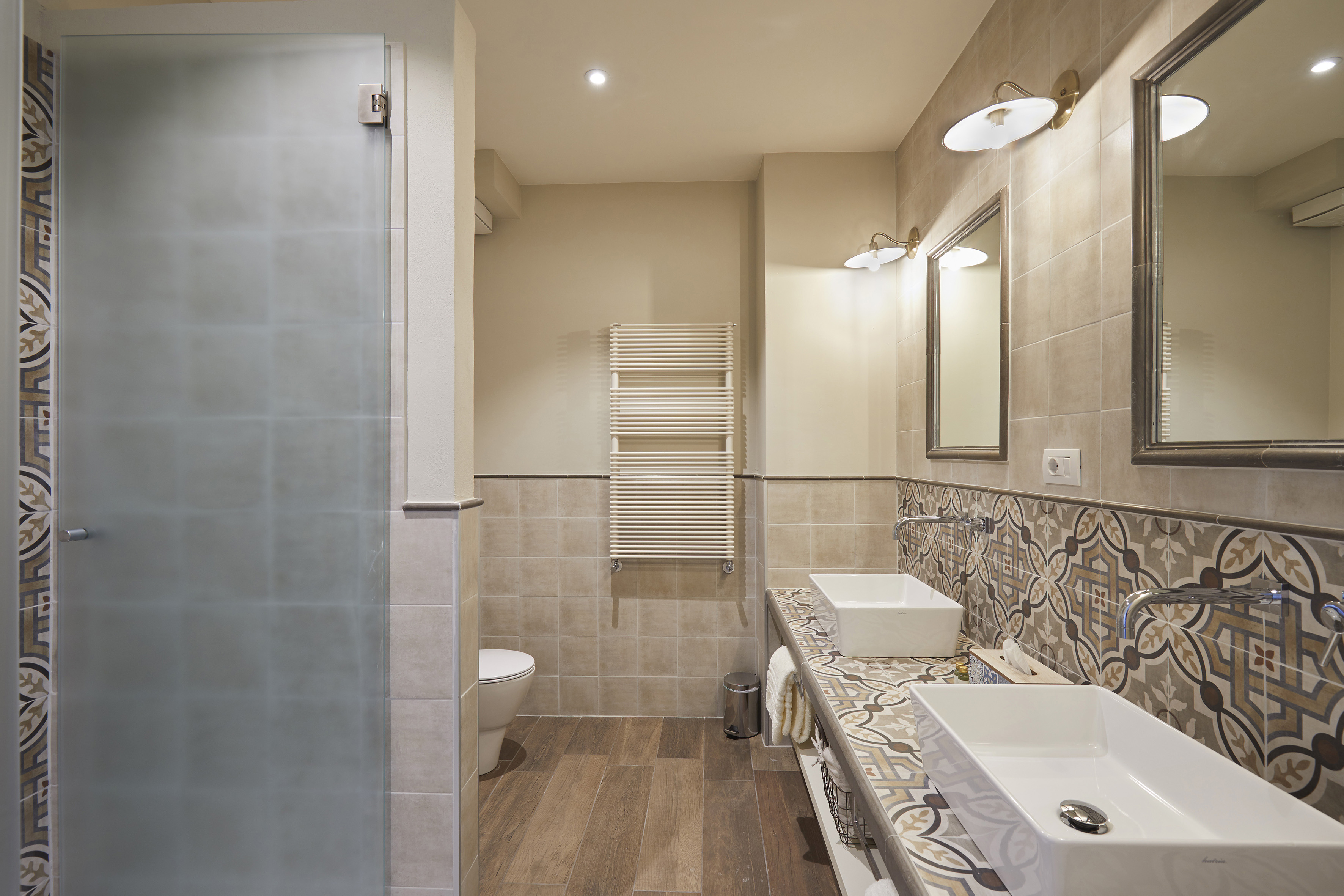 Modern bathroom with dual sinks, patterned tile counter, and frosted glass shower.