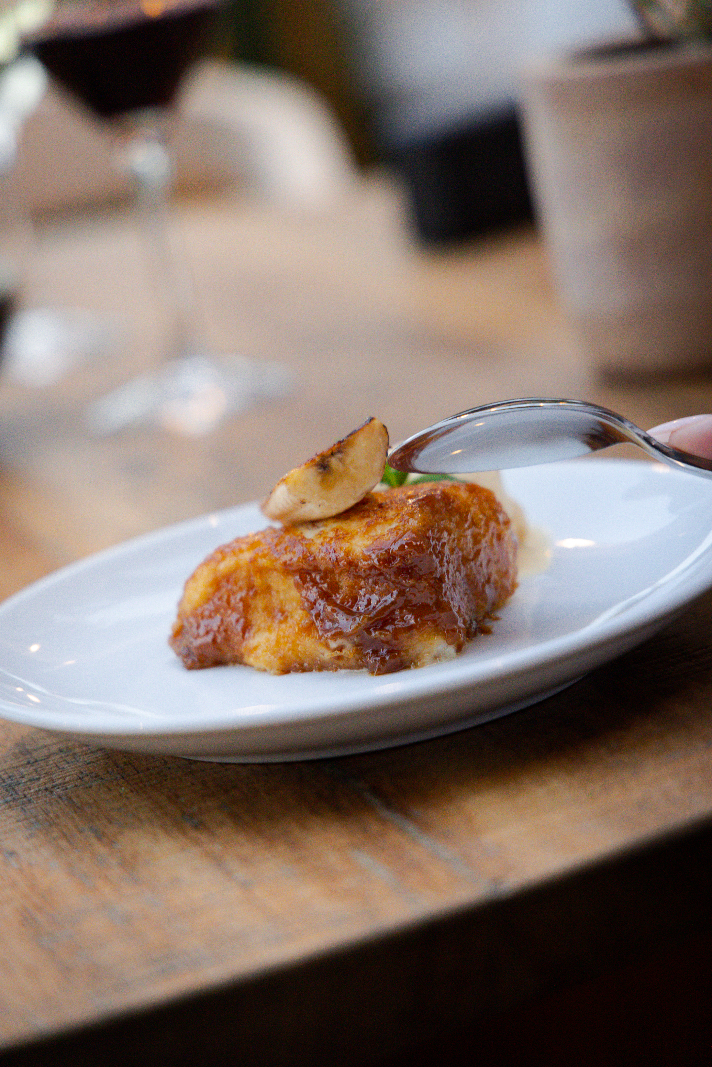 Caramelized French toast with banana on white plate, spoon poised.