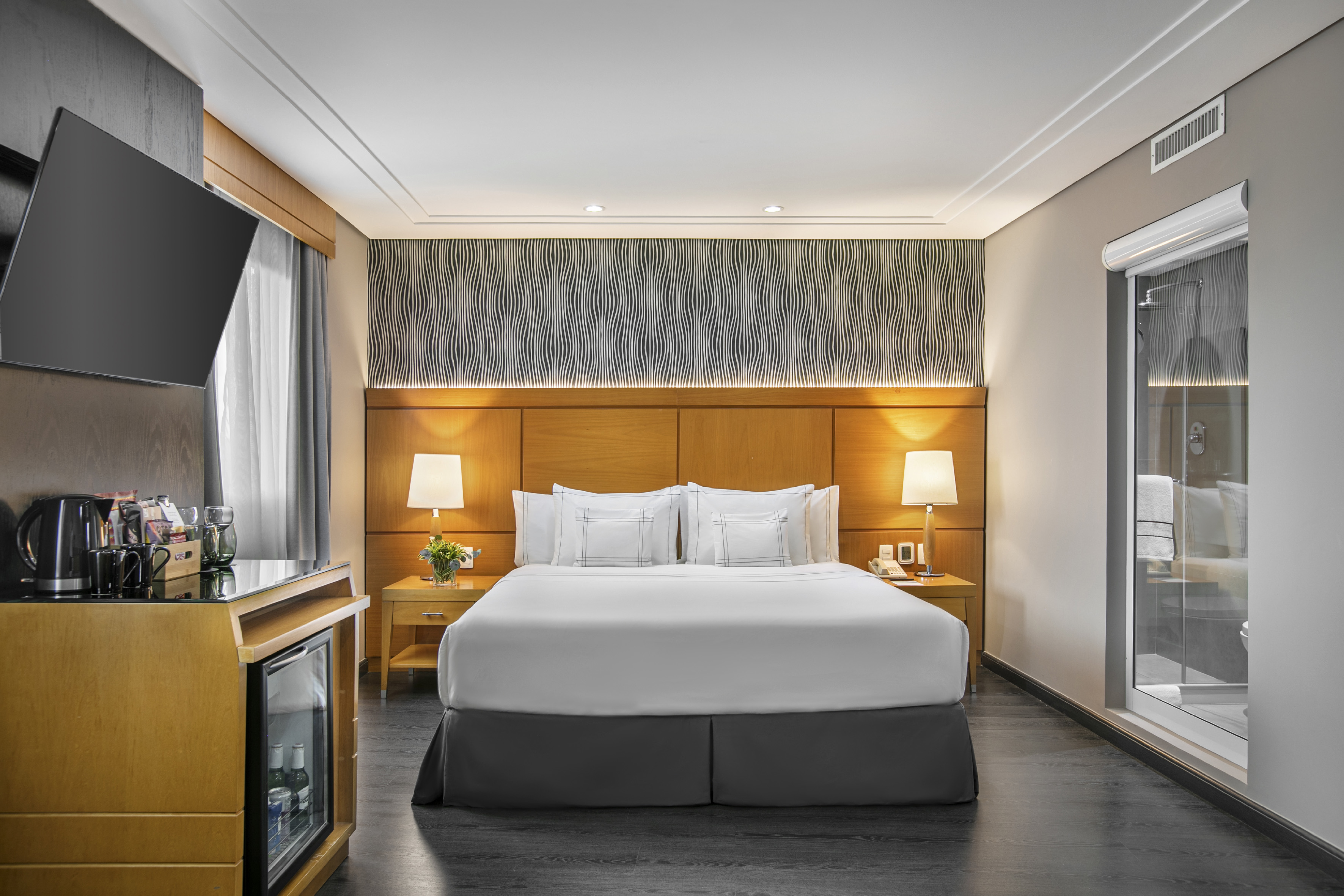 Modern hotel room with king bed, TV, minibar, and private bath.