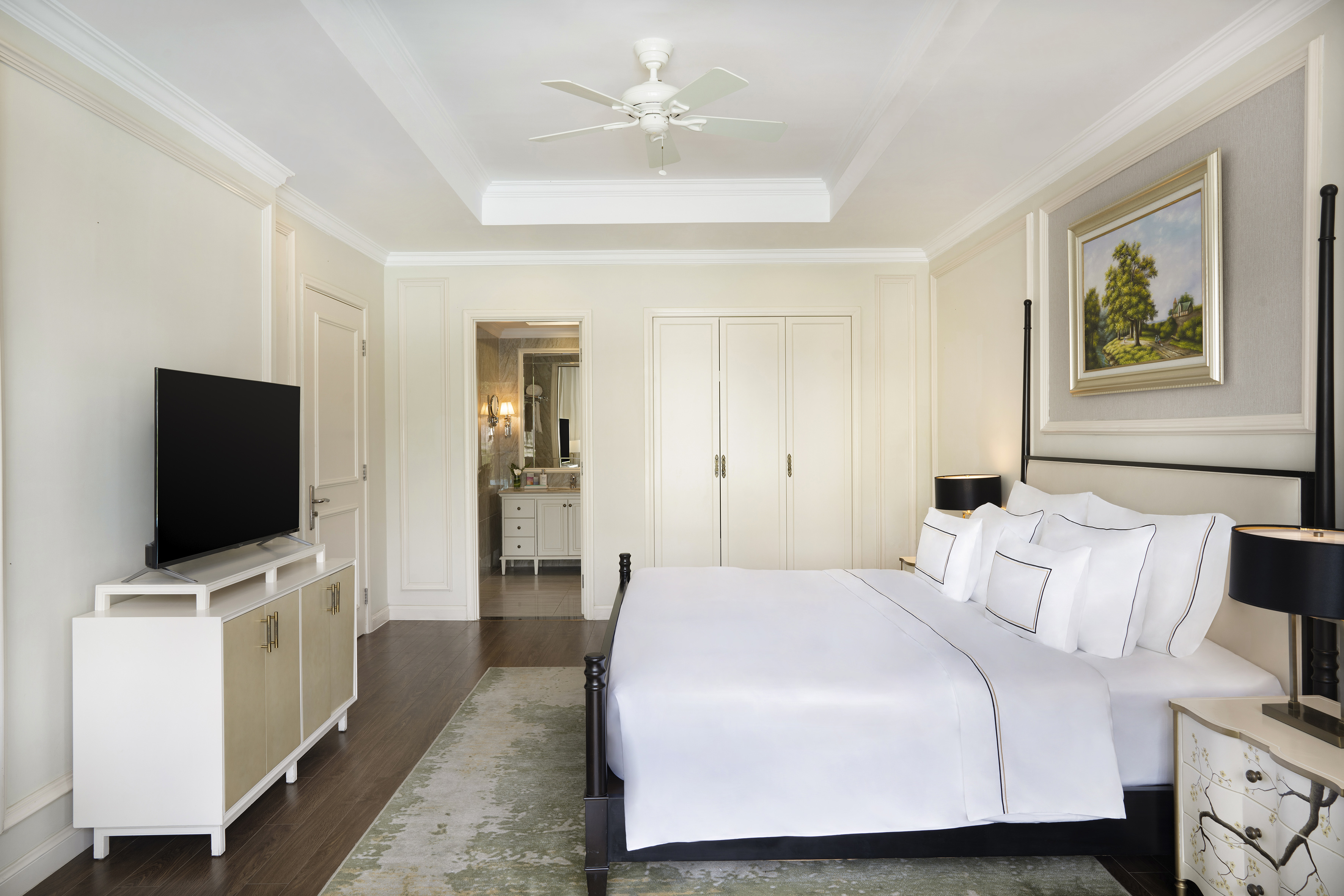 Elegant bedroom with white bedding, dark wood accents, TV, and en-suite bathroom.