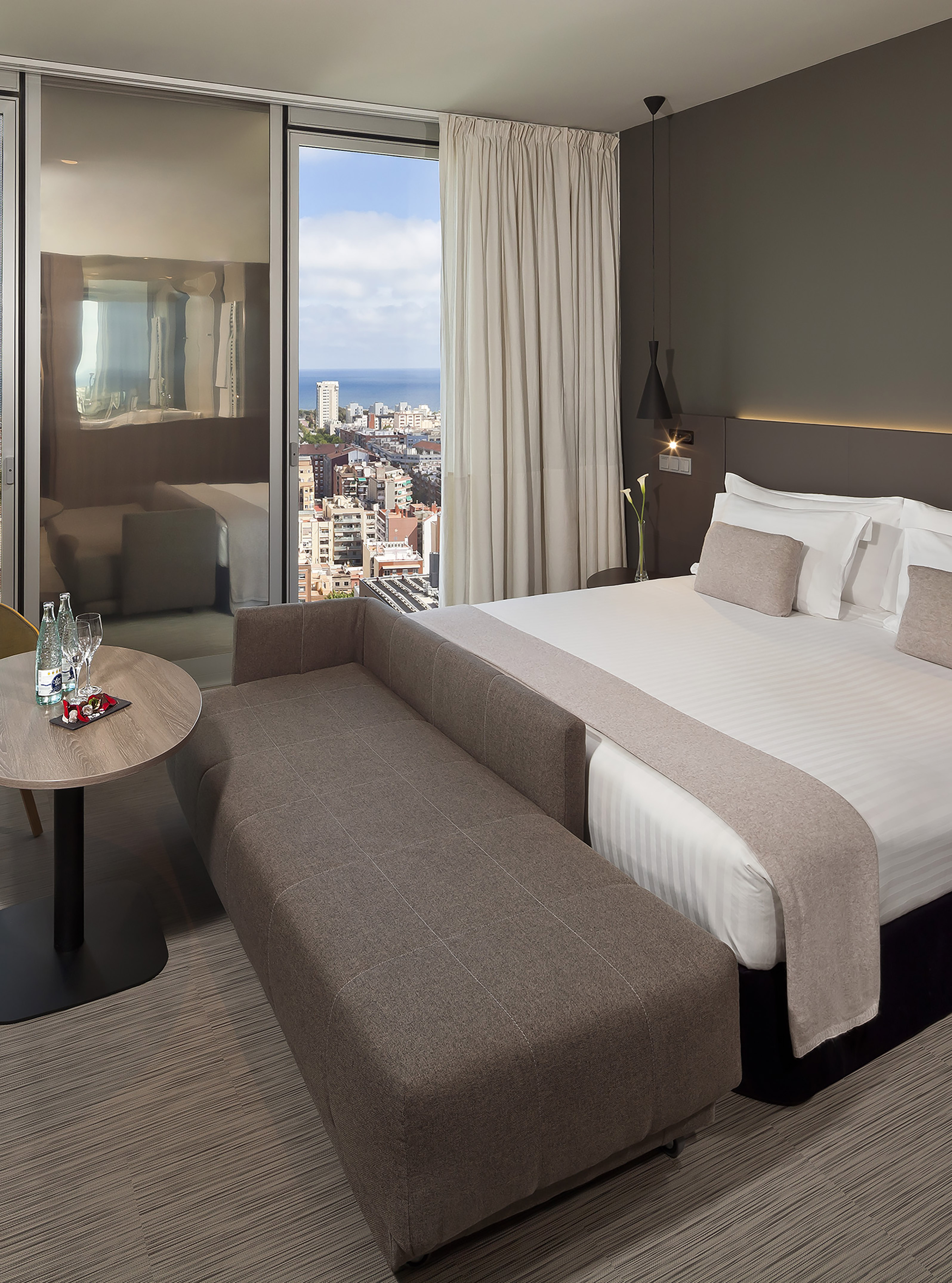 Luxurious hotel bedroom with ocean city view, large bed, and lounge seating.