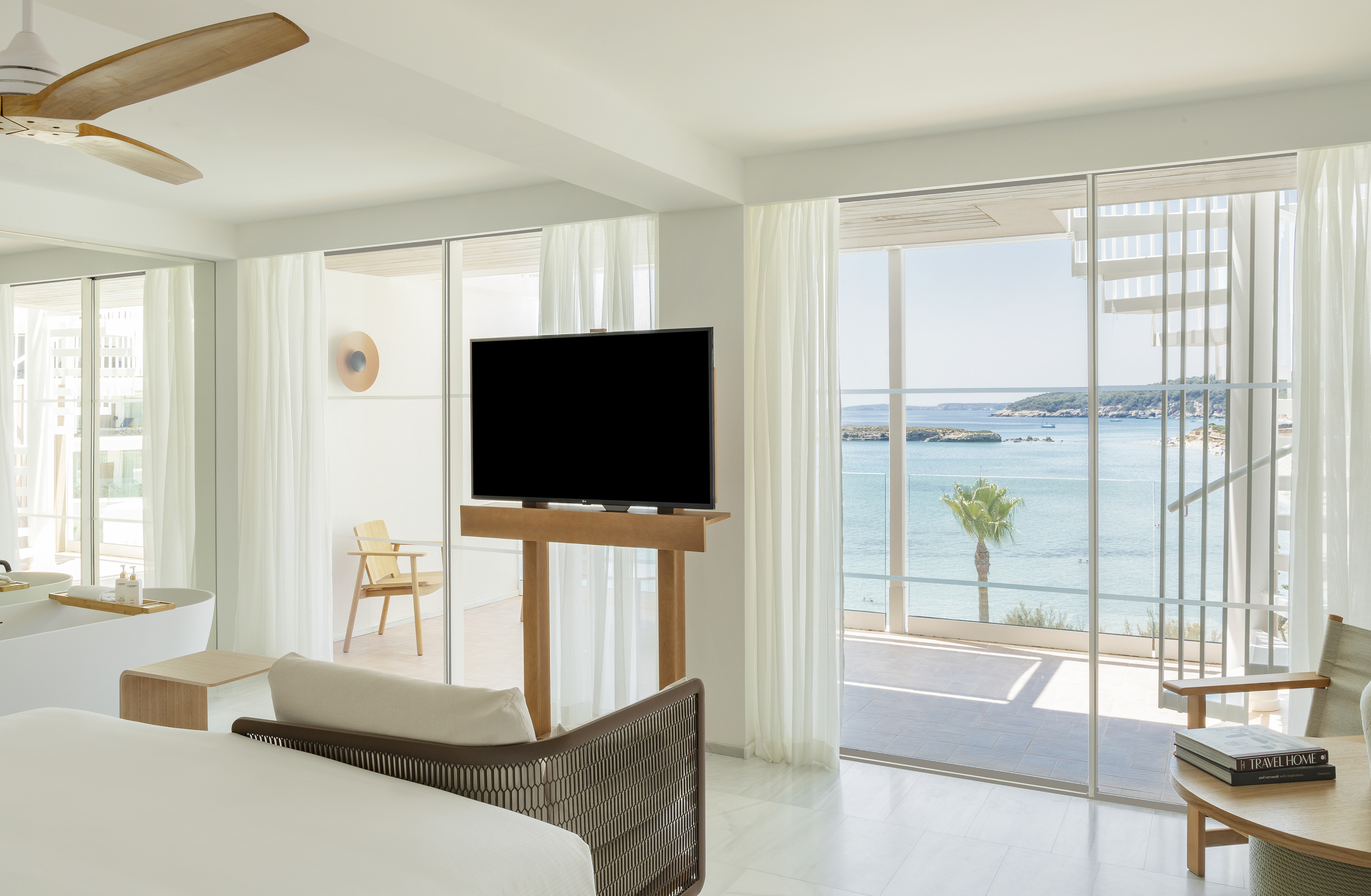 Luxury hotel room with sea view, modern white decor, large windows, balcony.
