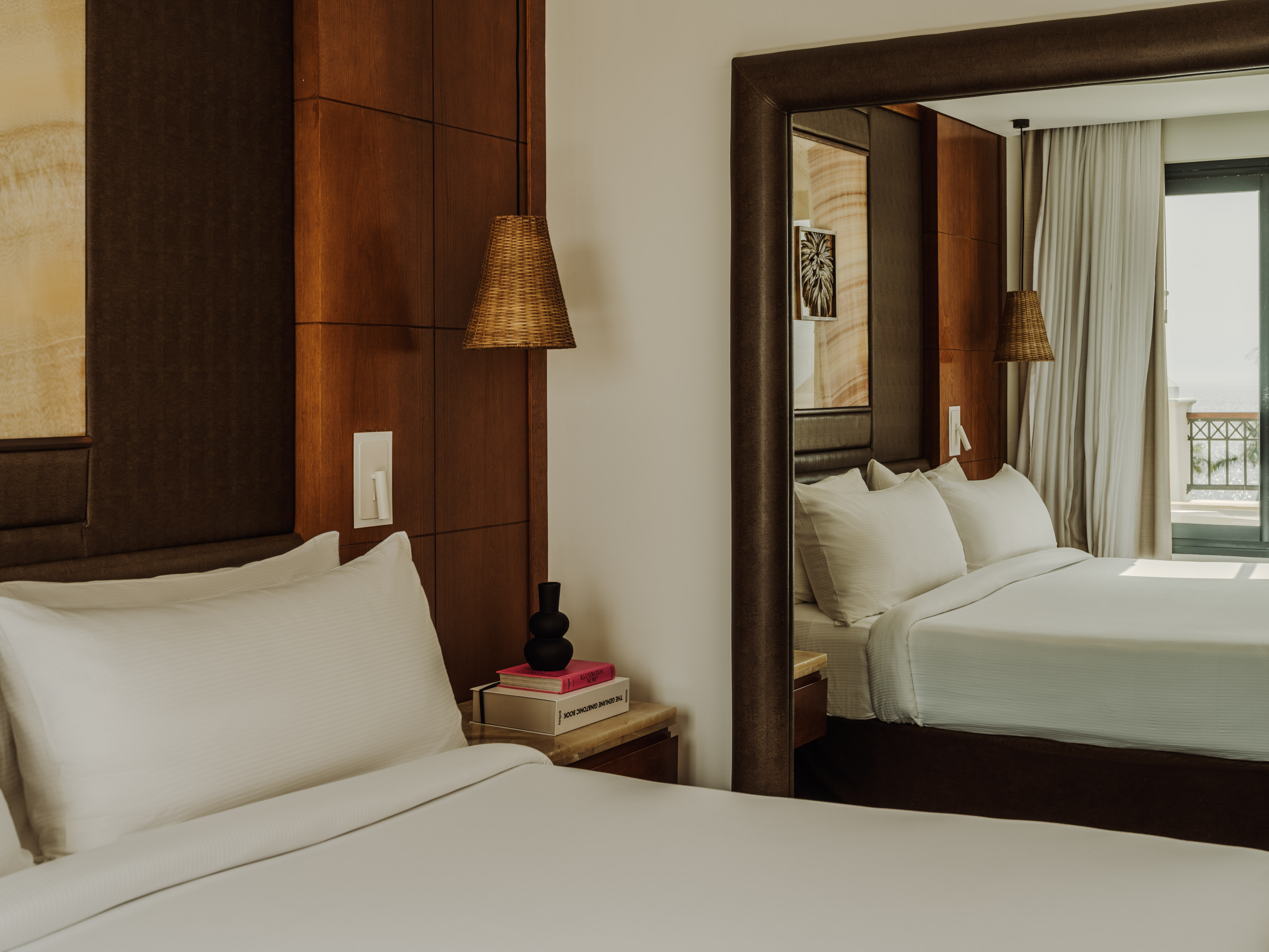 Modern hotel bedroom with white bed, wood paneling, nightstand, and mirror.