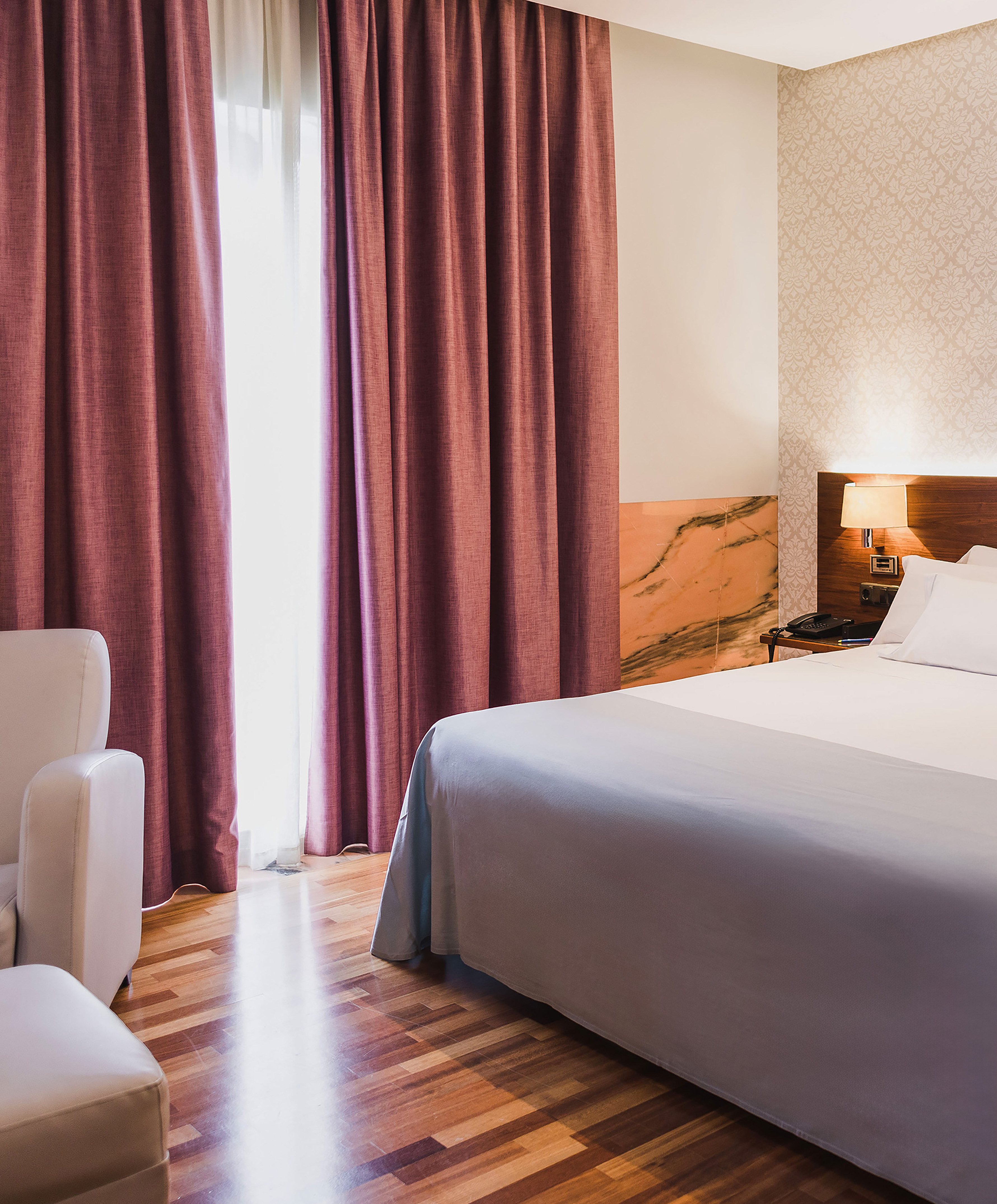 a bed with a lamp and a chair in a room with pink curtains