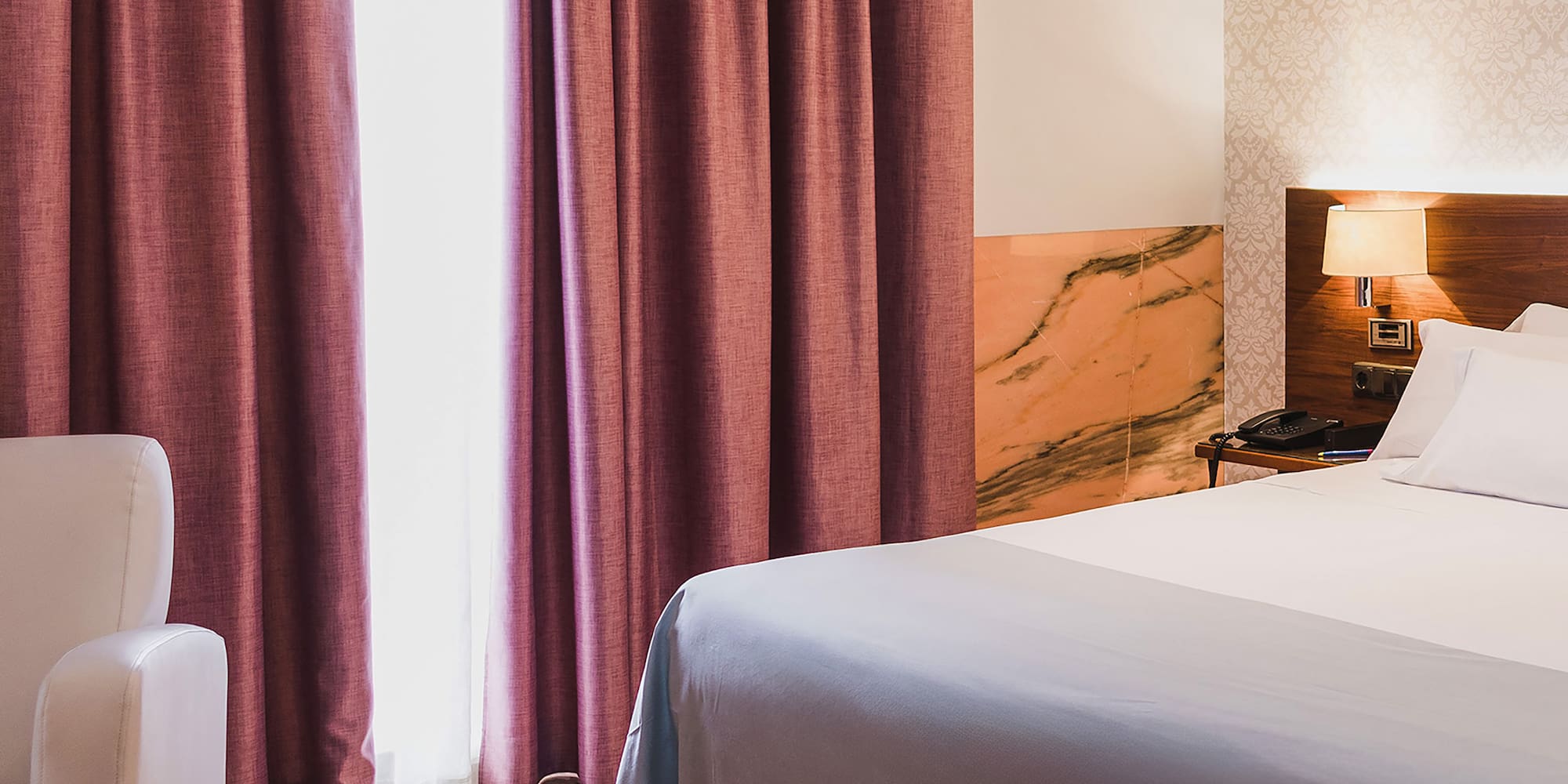 a bed with a lamp and a chair in a room with pink curtains