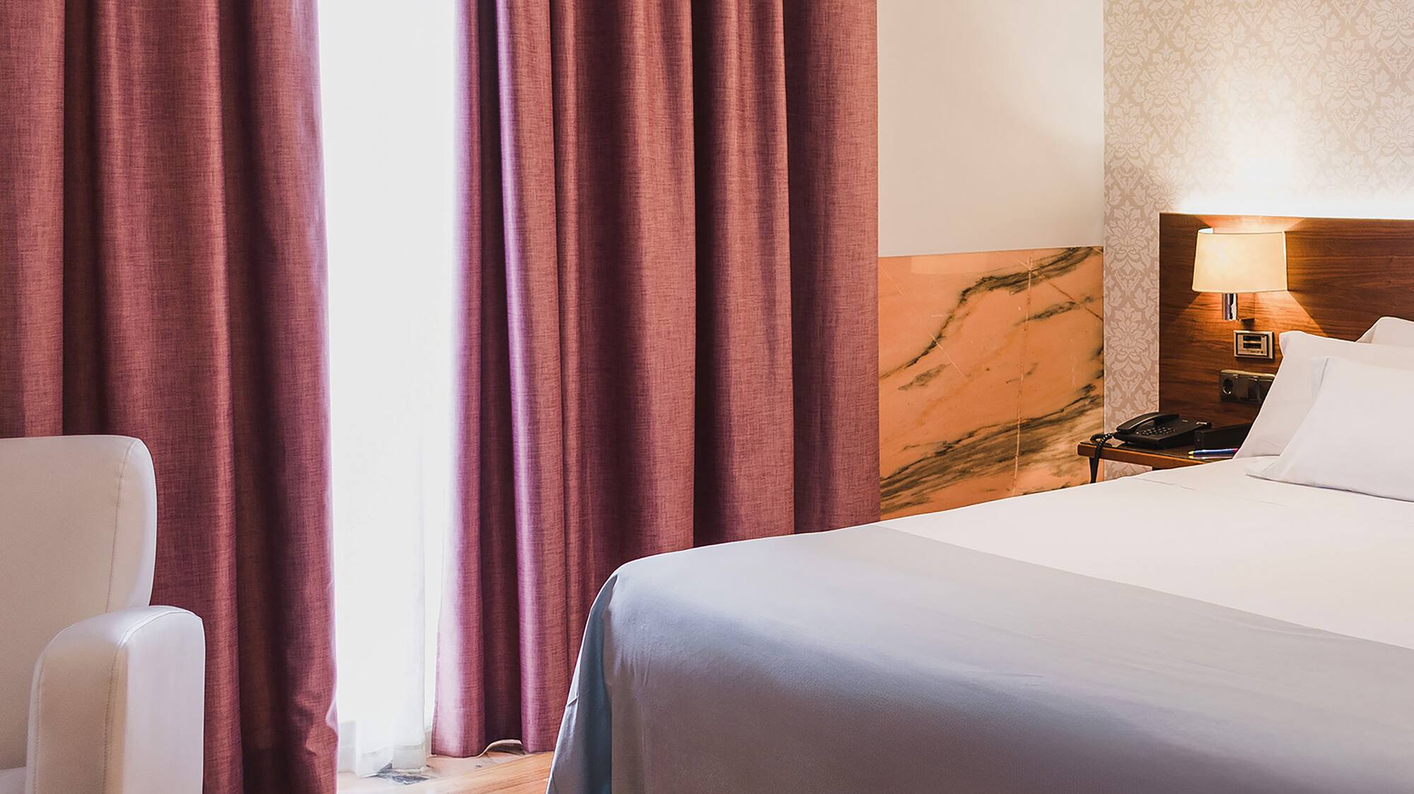 a bed with a lamp and a chair in a room with pink curtains