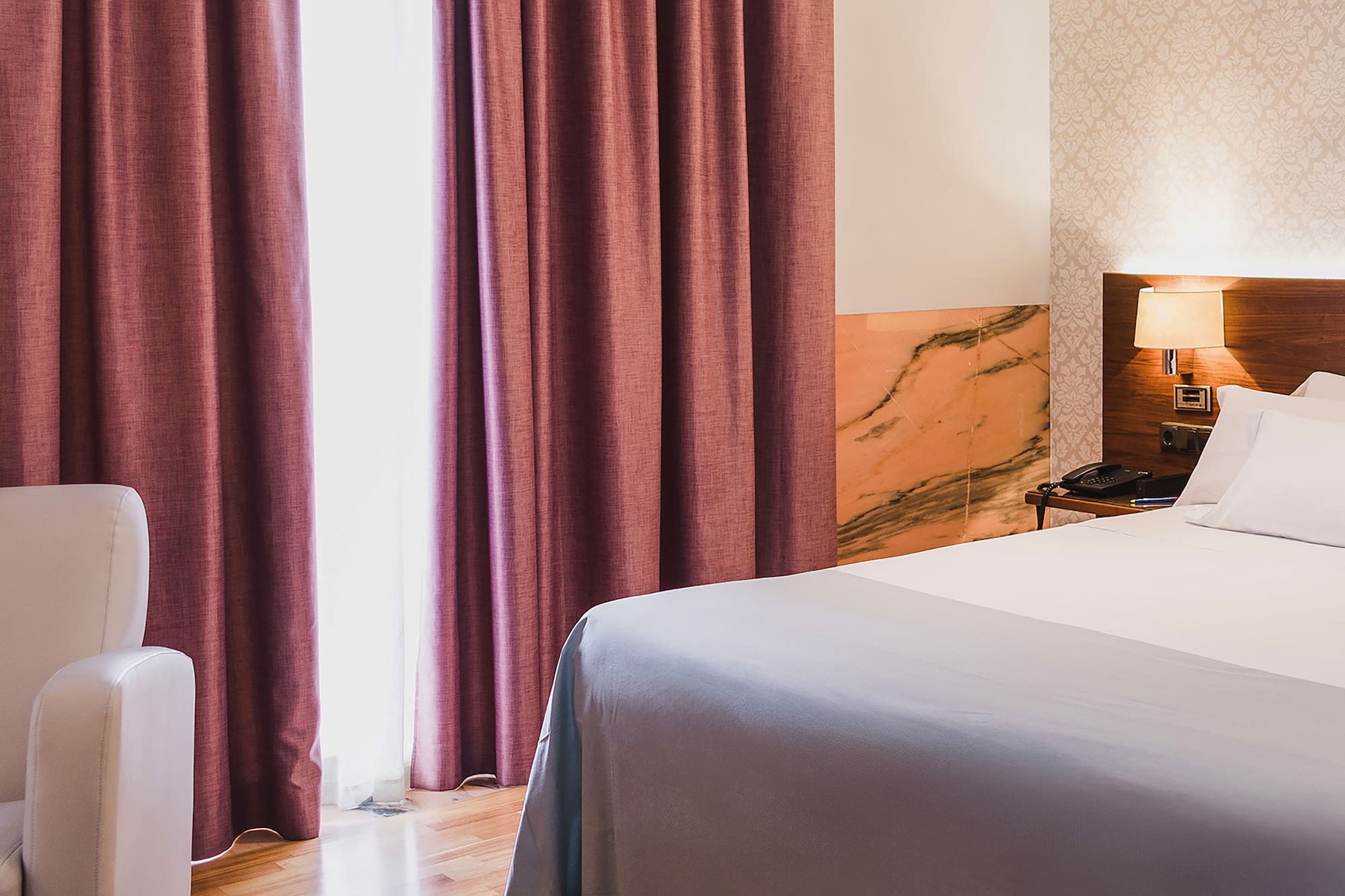 a bed with a lamp and a chair in a room with pink curtains