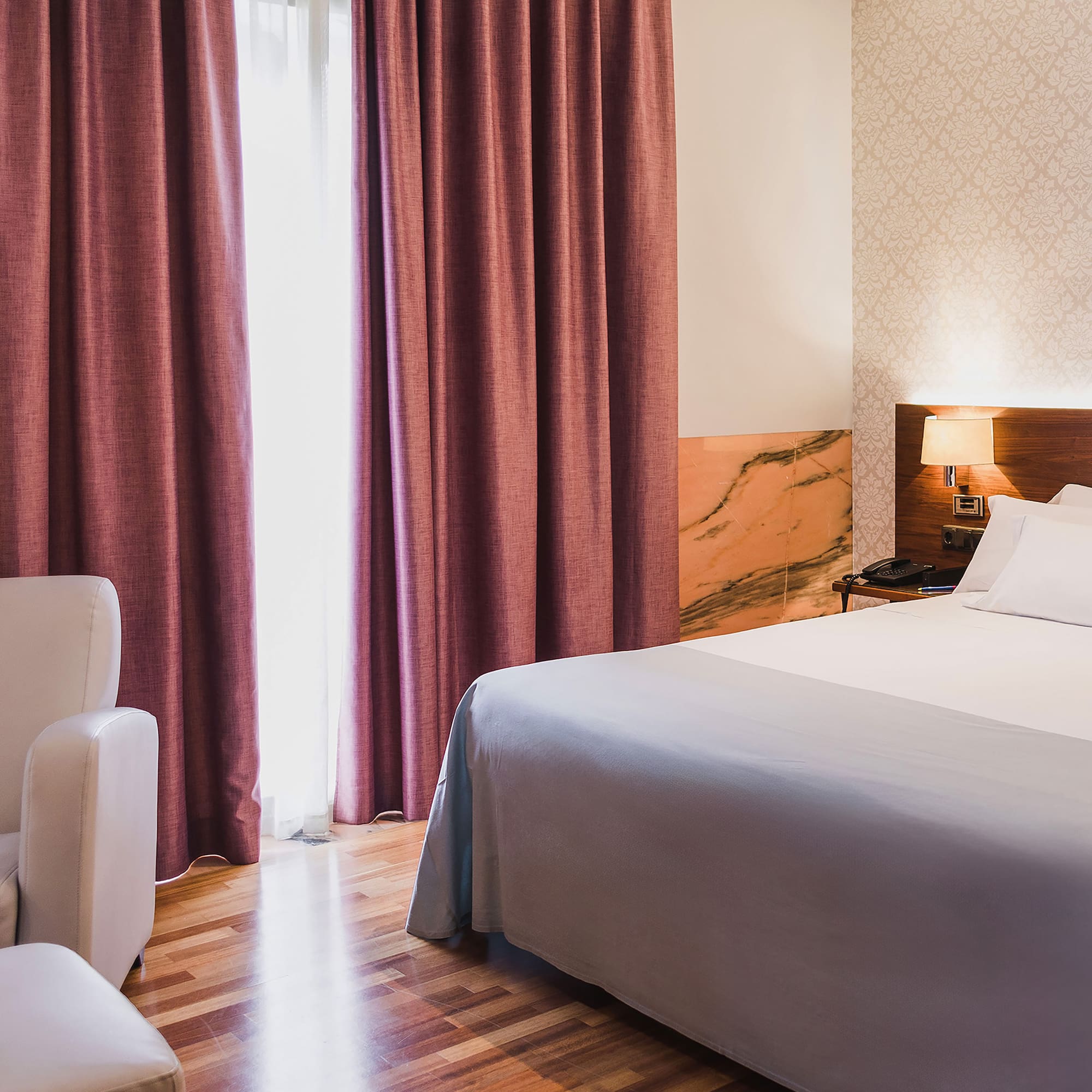 a bed with a lamp and a chair in a room with pink curtains