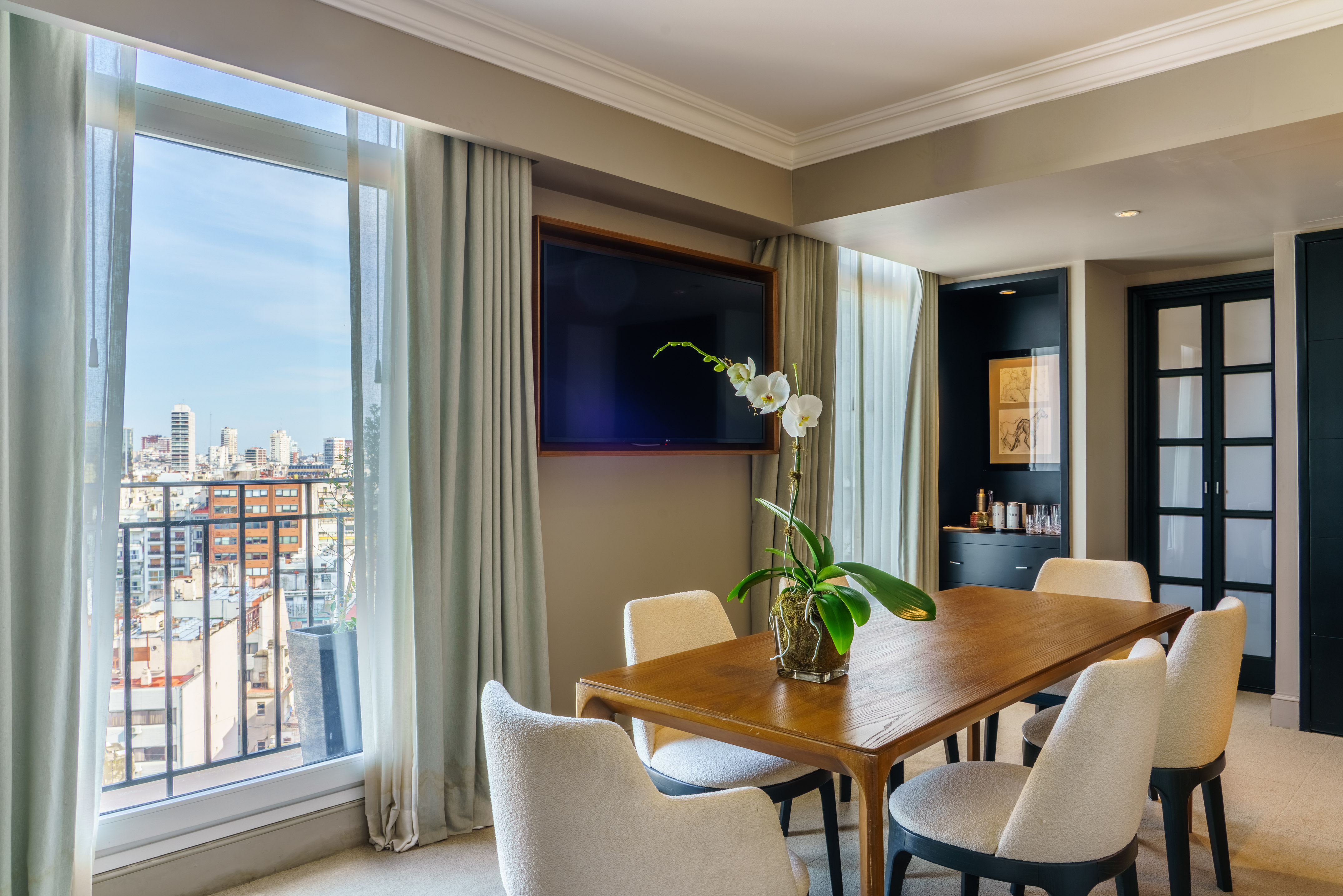 Dining area with city view, wooden table, white chairs, and wall-mounted TV.