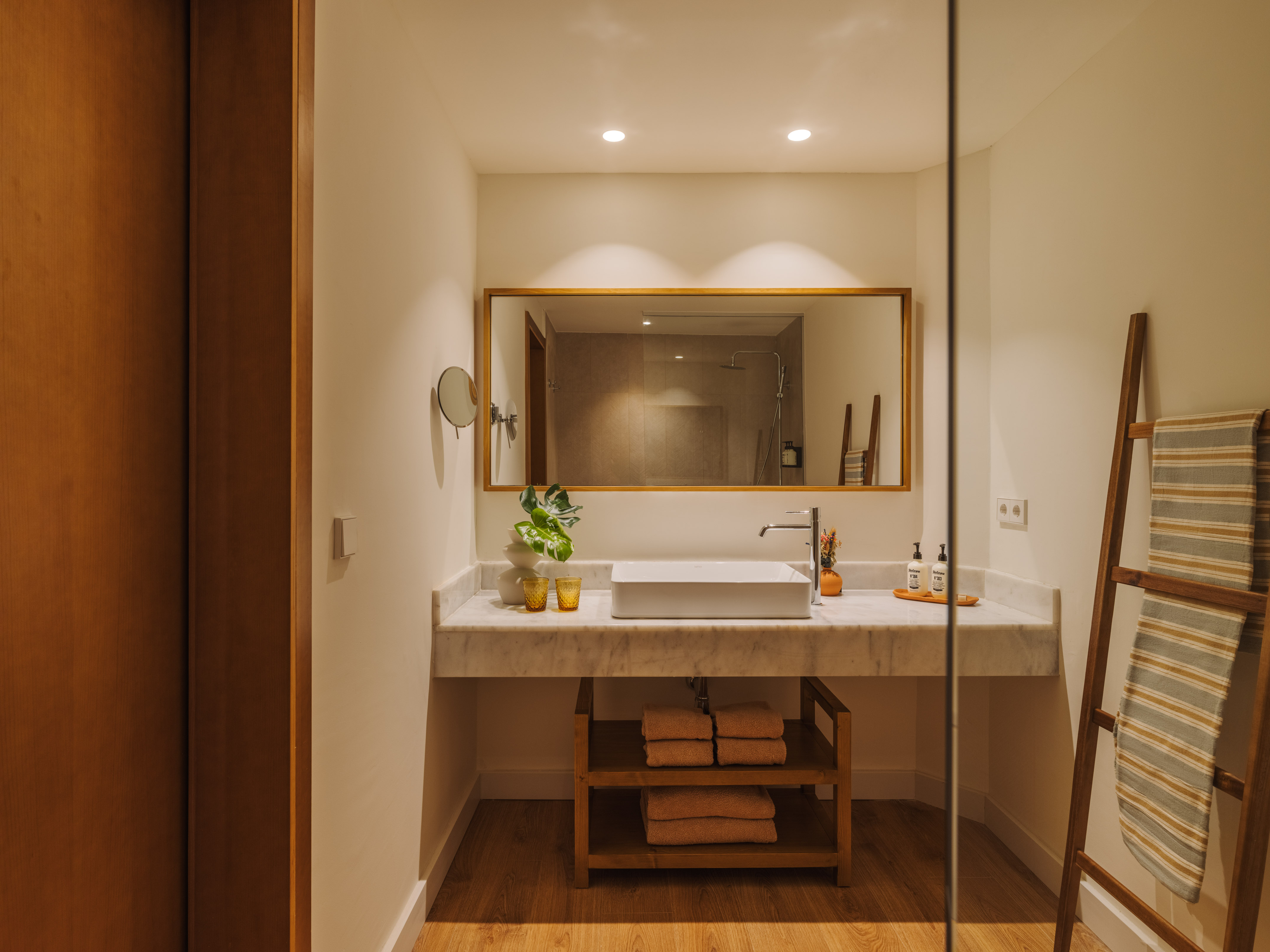 Modern bathroom vanity with marble counter, white sink, wood mirror, and towel ladder.