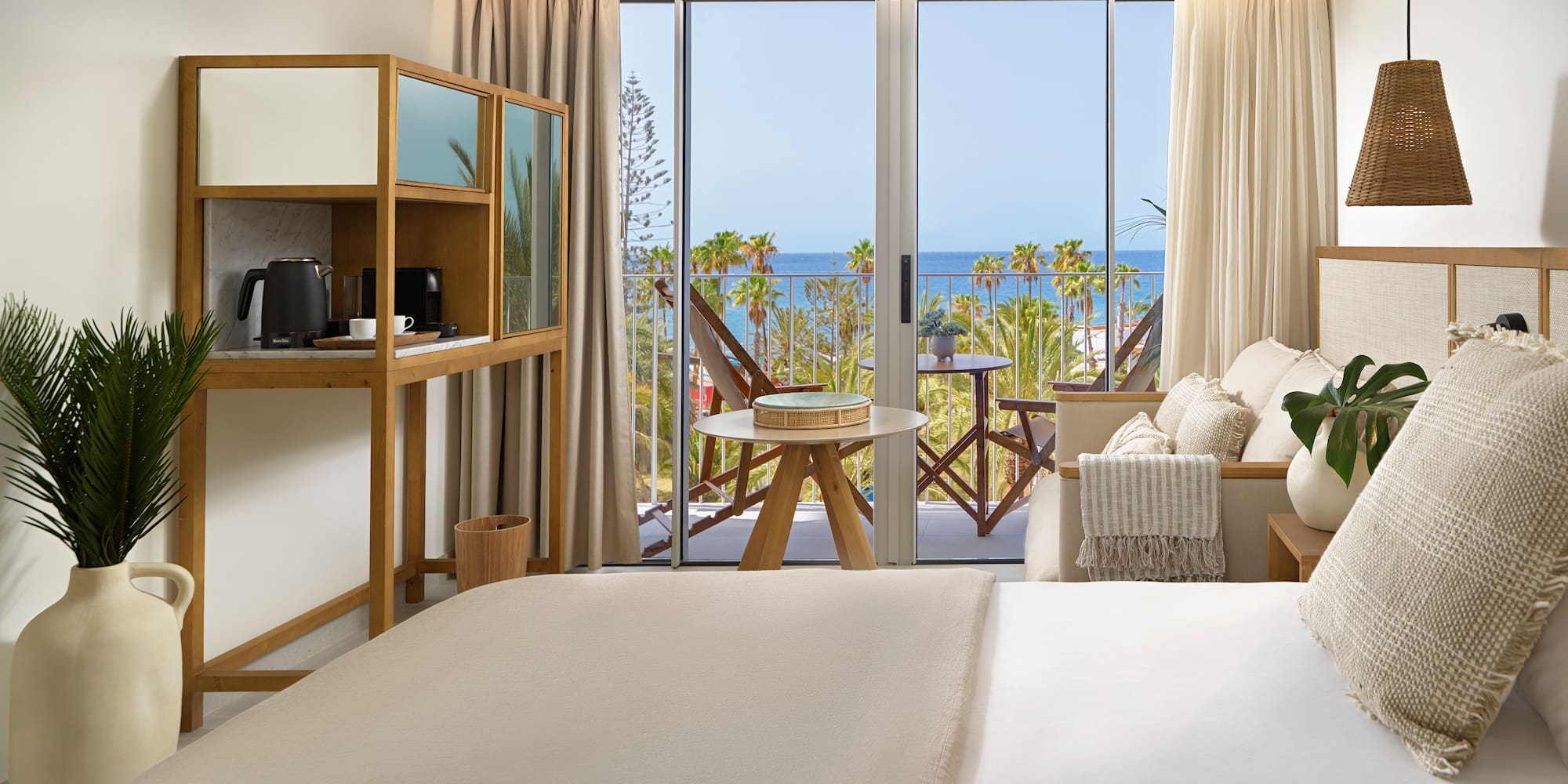 a room with a bed and a table and chairs and a balcony with a view of the ocean