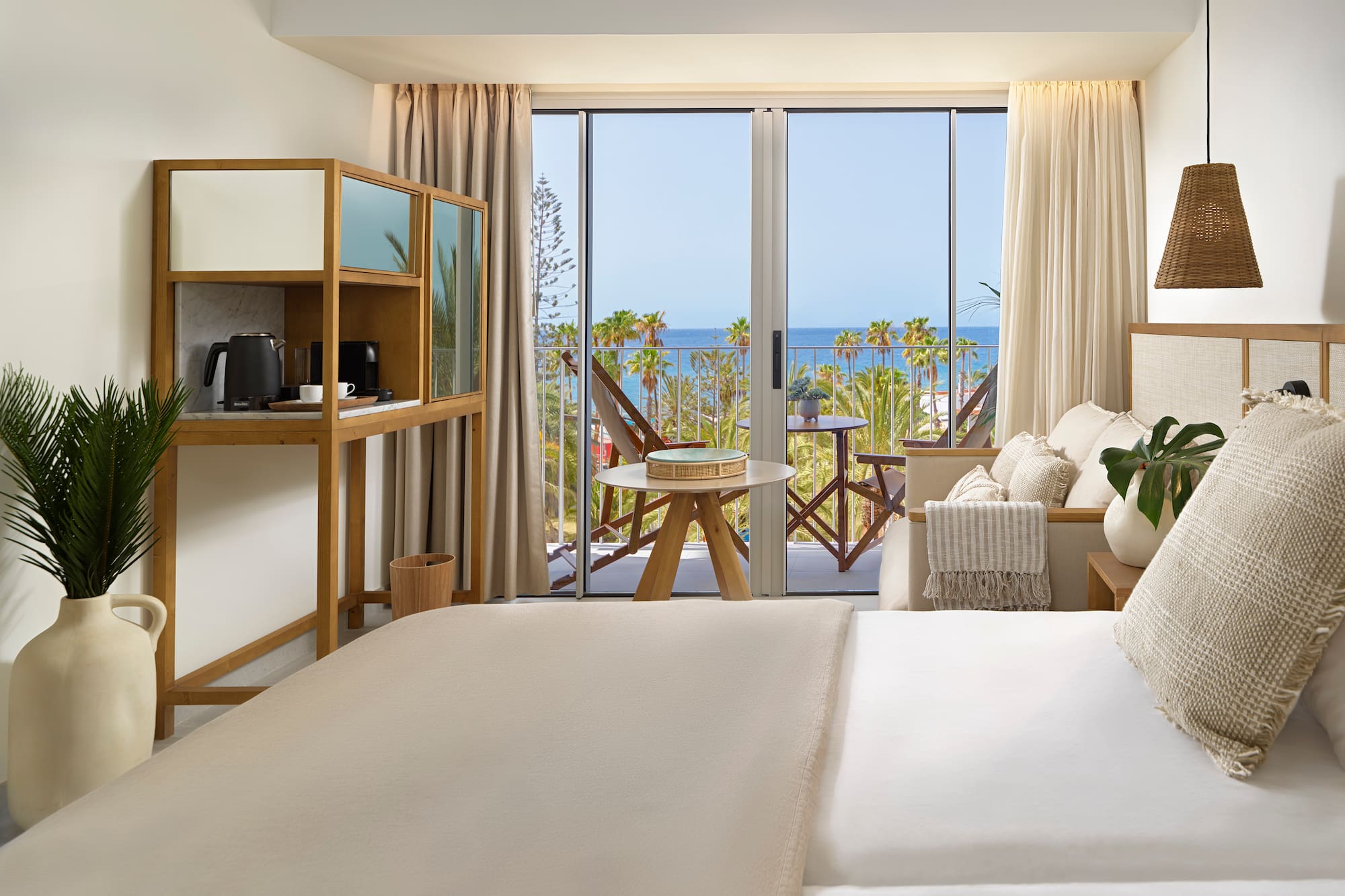 a room with a bed and a table and chairs and a balcony with a view of the ocean