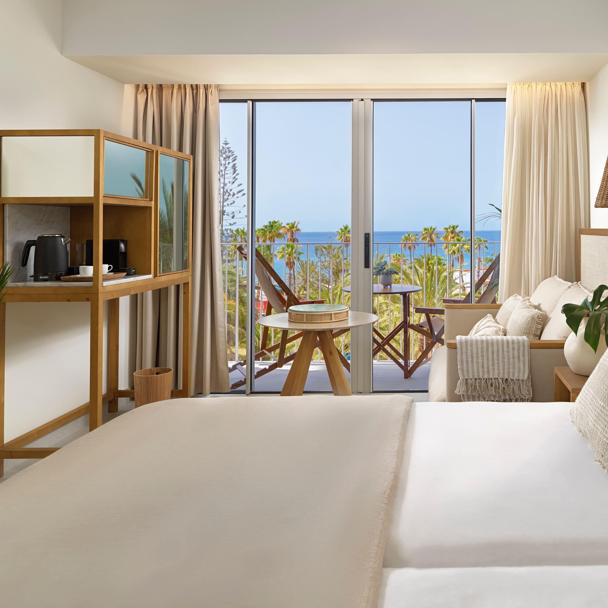 a room with a bed and a table and chairs and a balcony with a view of the ocean