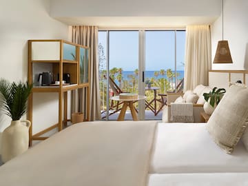 a room with a bed and a table and chairs and a balcony with a view of the ocean