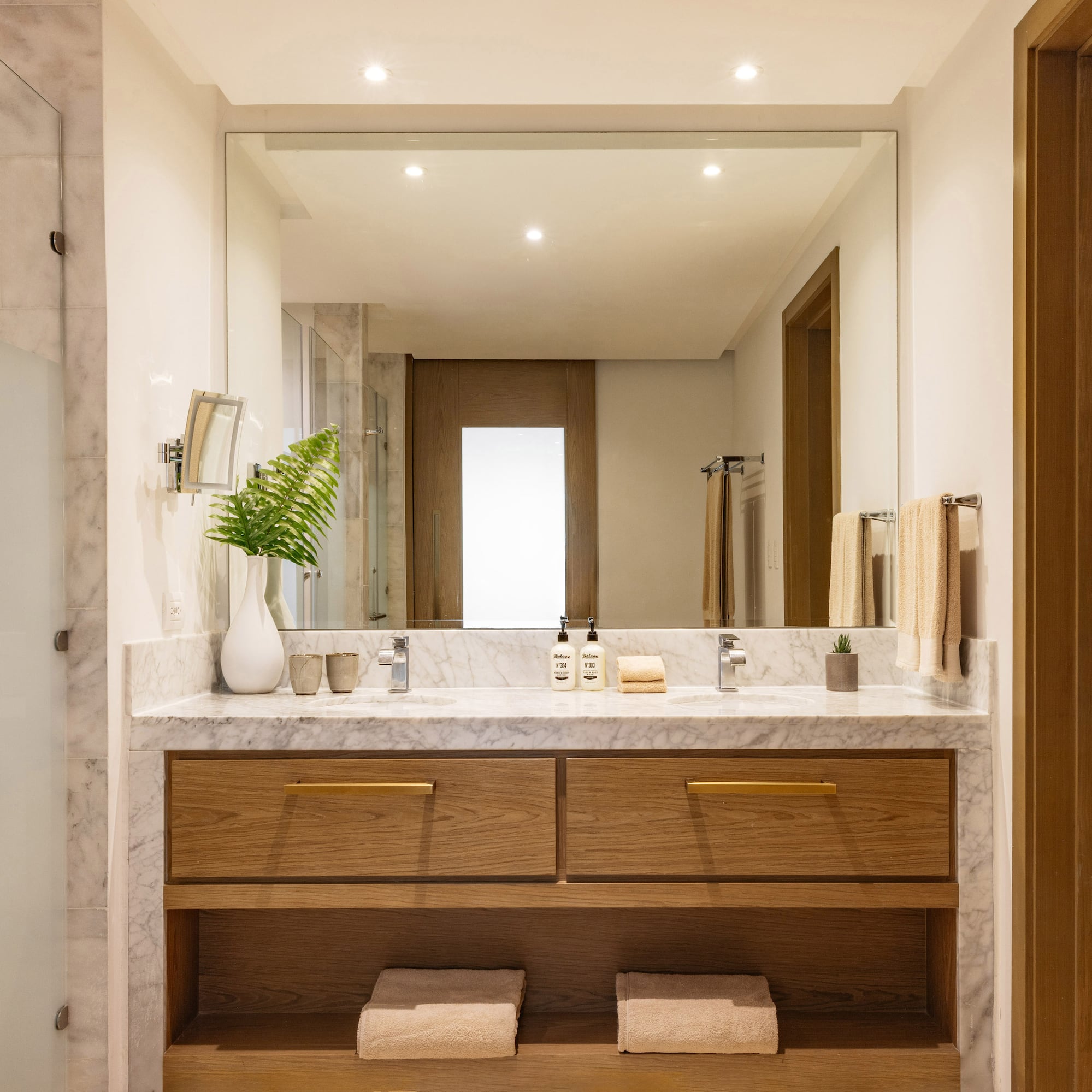 Modern bathroom with marble double vanity, wood cabinets, and large mirror.