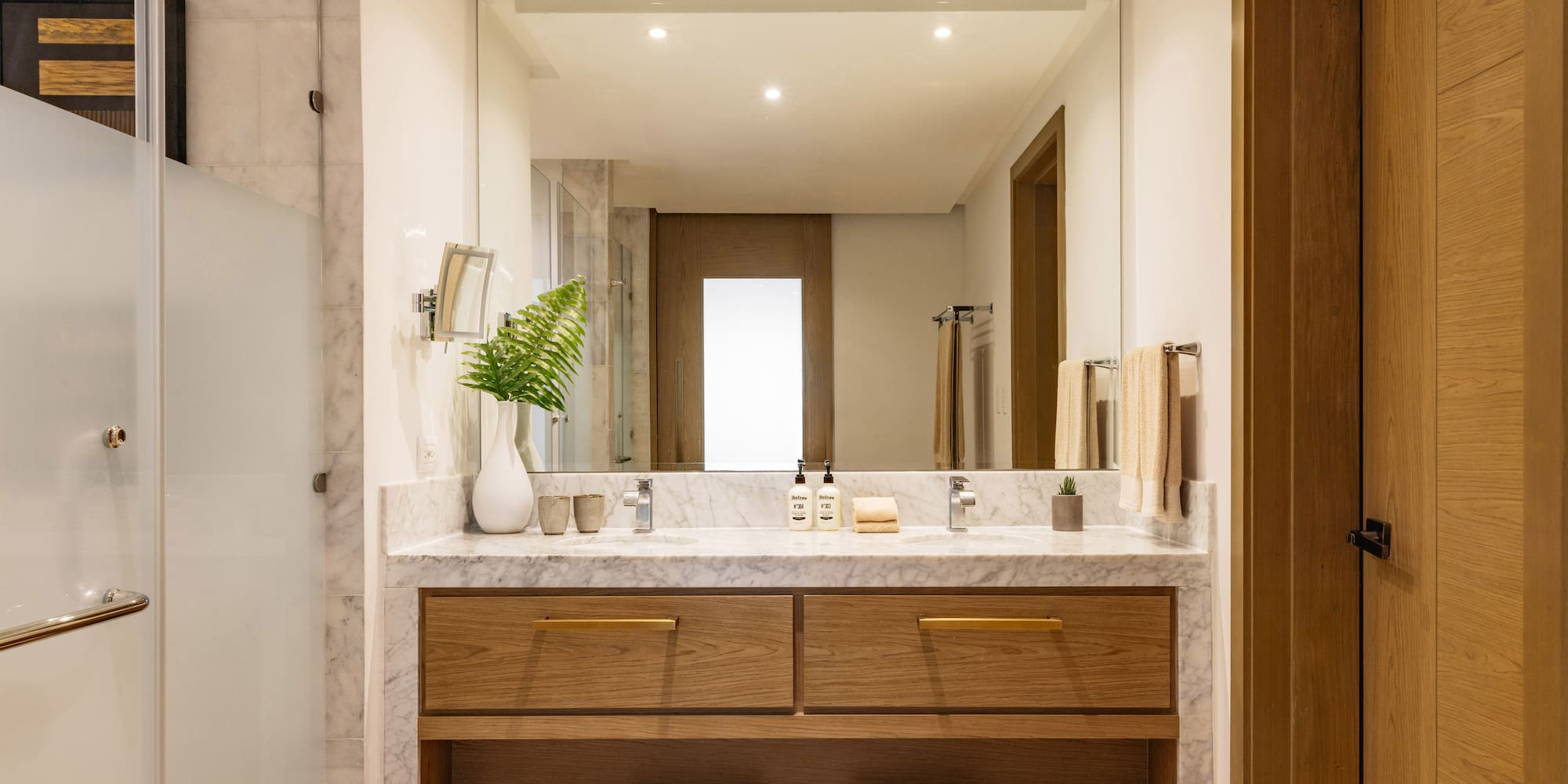 Modern hotel bathroom with marble double vanity, wood cabinets, and large mirror.