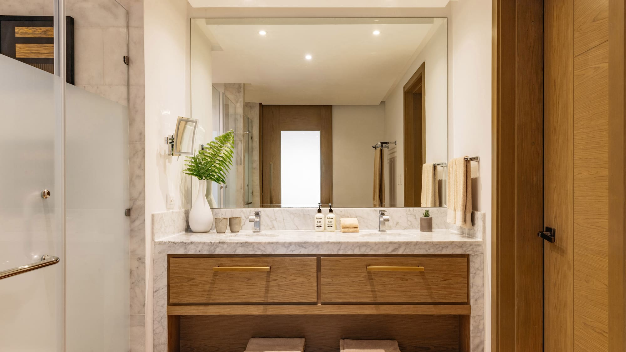 Modern bathroom with marble double vanity, wood cabinets, and large mirror.