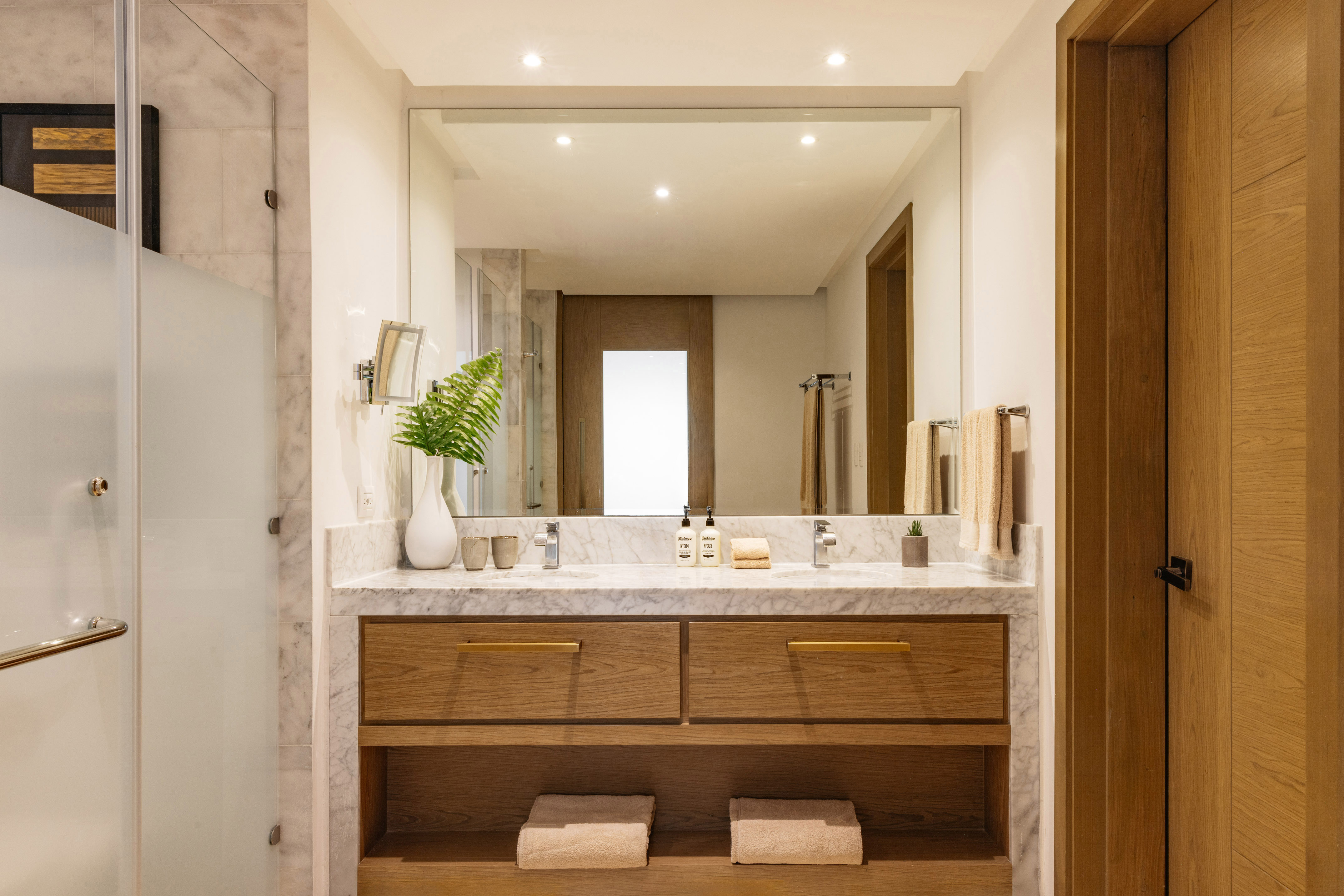 Modern hotel bathroom with marble double vanity, wood cabinets, and large mirror.