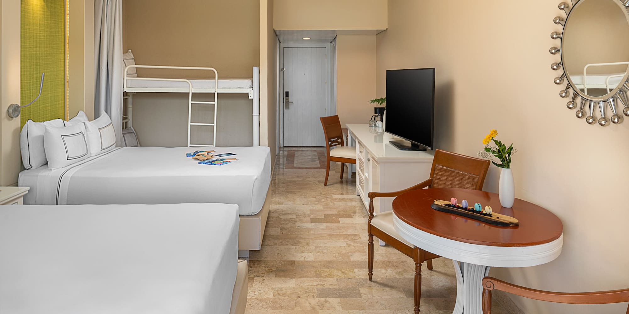 Family hotel room with two large beds, bunk beds, TV, desk, and dining area.