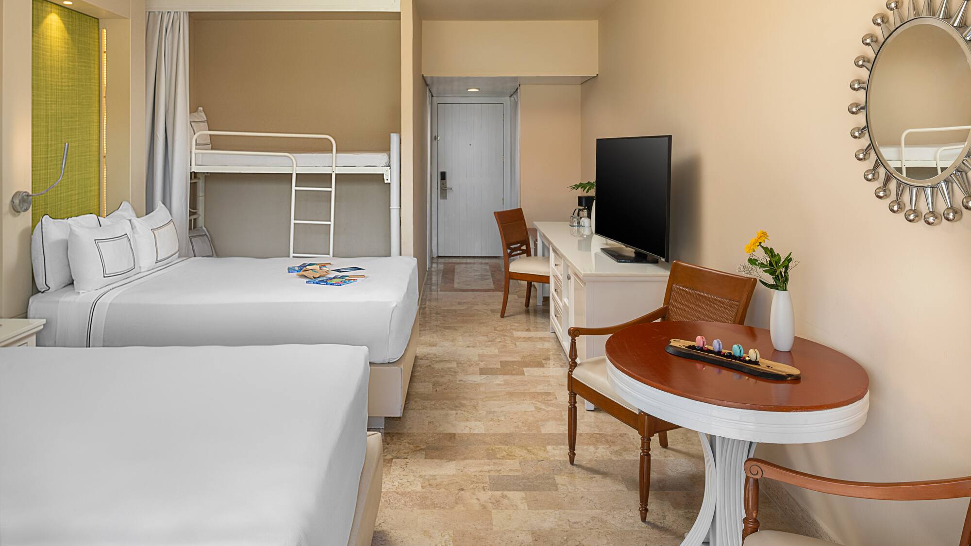 Spacious family hotel room with two beds, bunk bed, TV, and dining area.