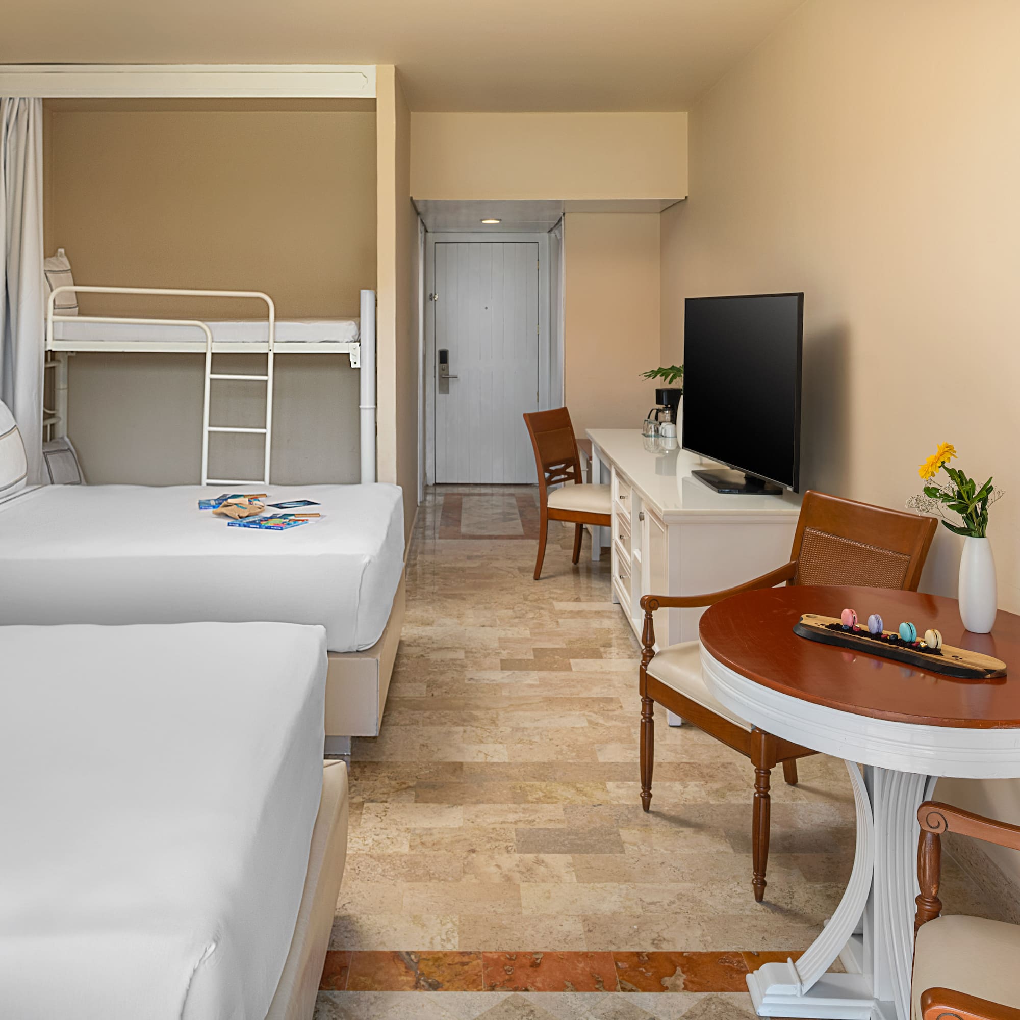Spacious family hotel room with two beds, bunk bed, TV, and dining area.