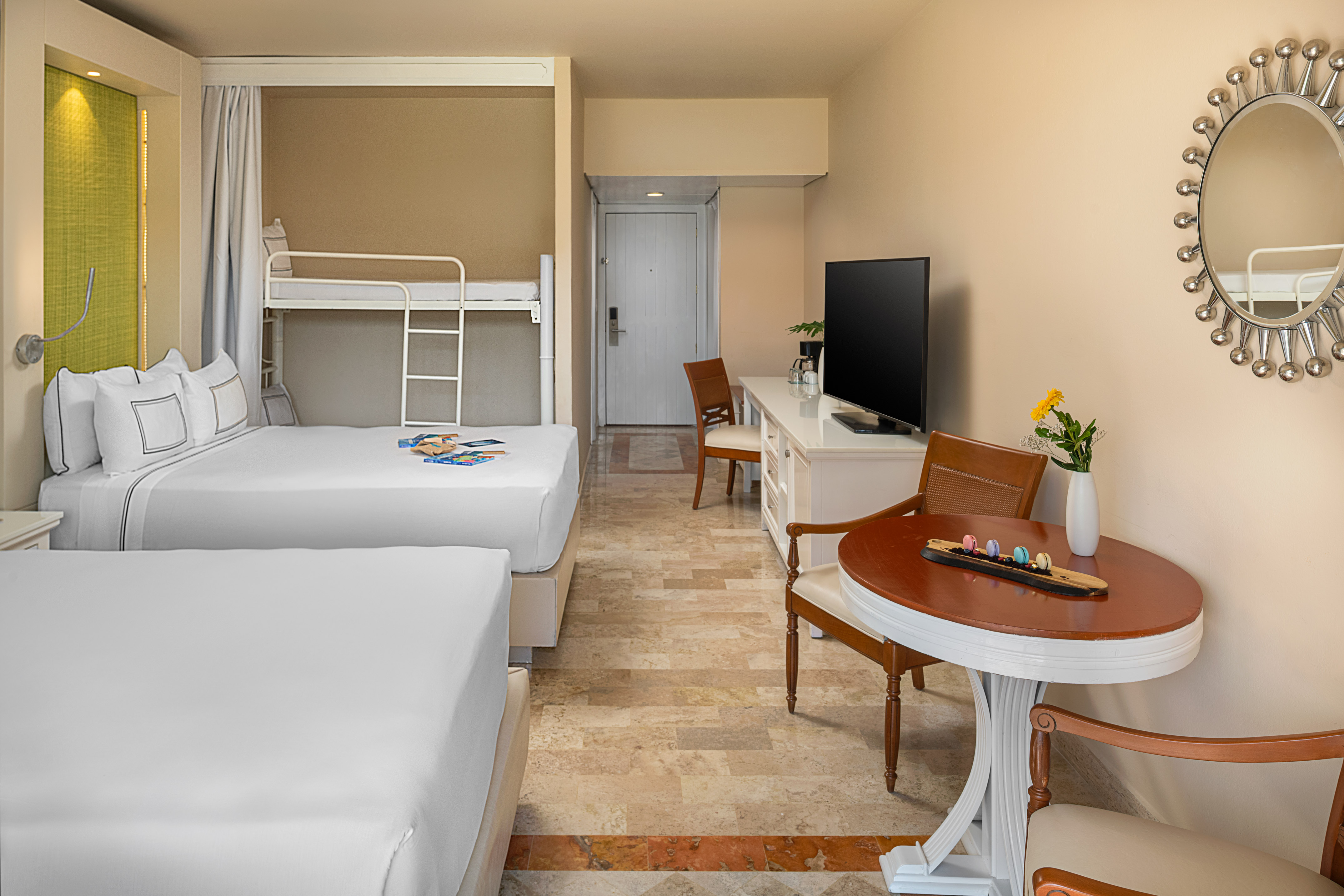 Family hotel room with two large beds, bunk beds, TV, desk, and dining area.