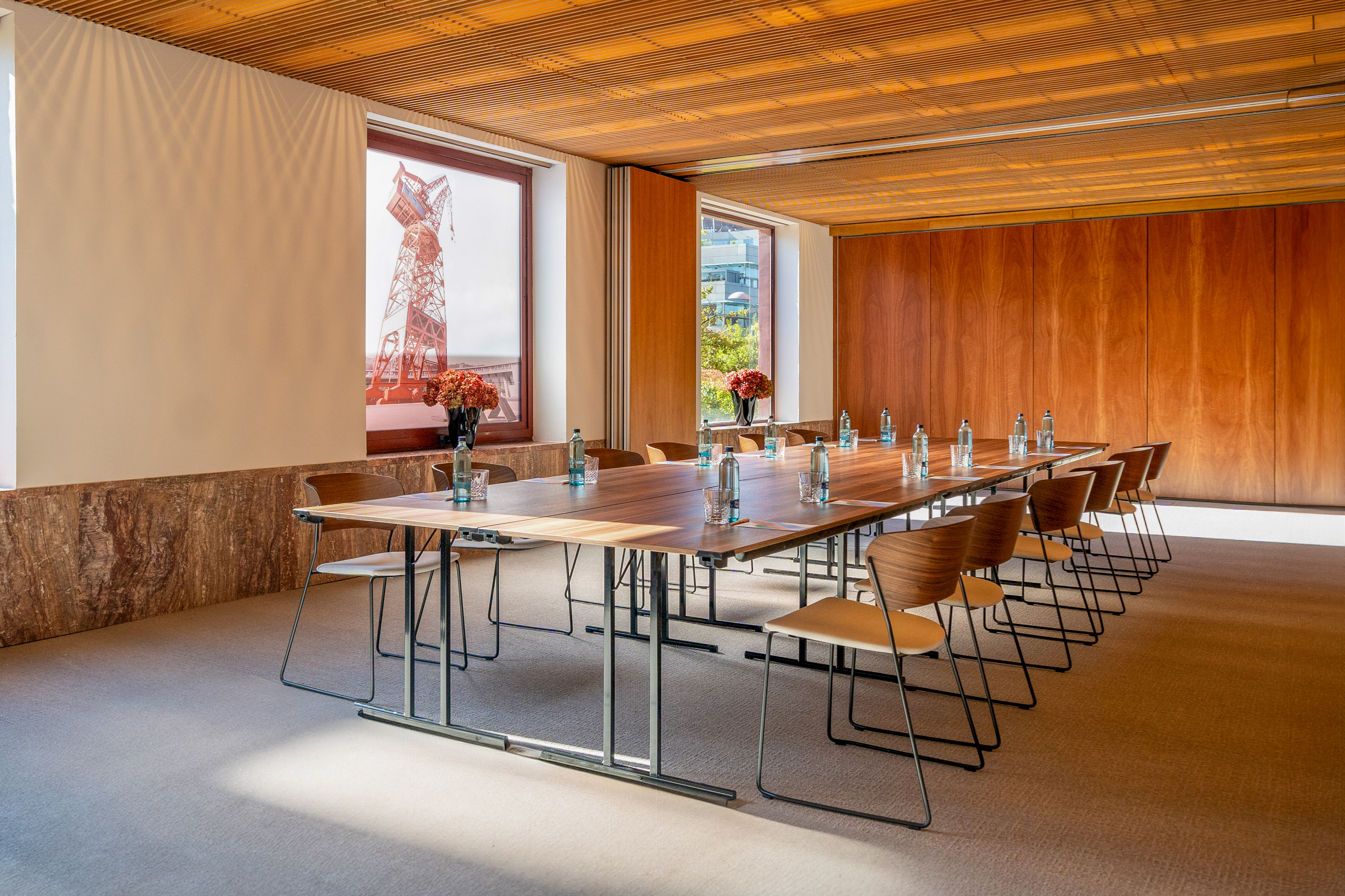 Modern conference room, large wooden table, chairs, natural light, city view.