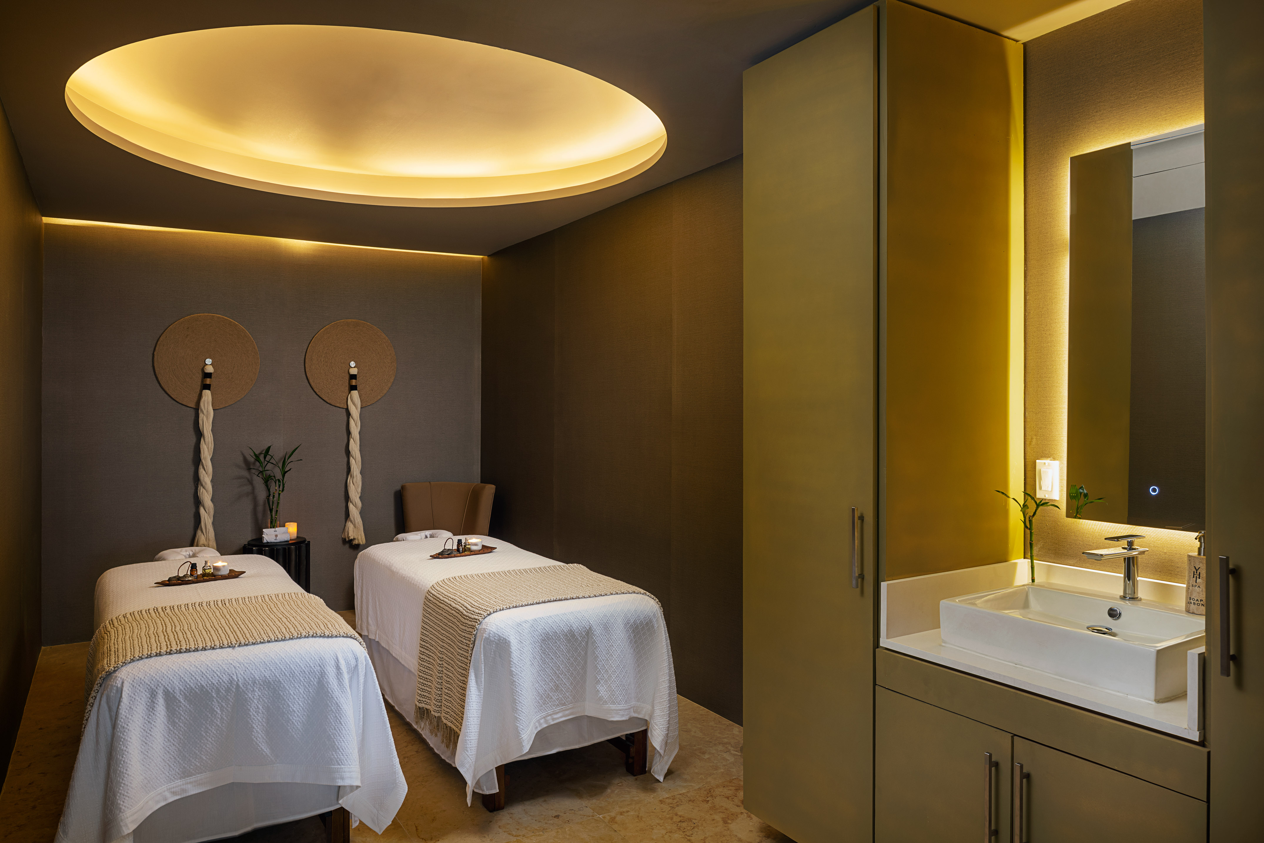 Luxury spa room with two massage beds, indirect lighting, and a modern vanity.